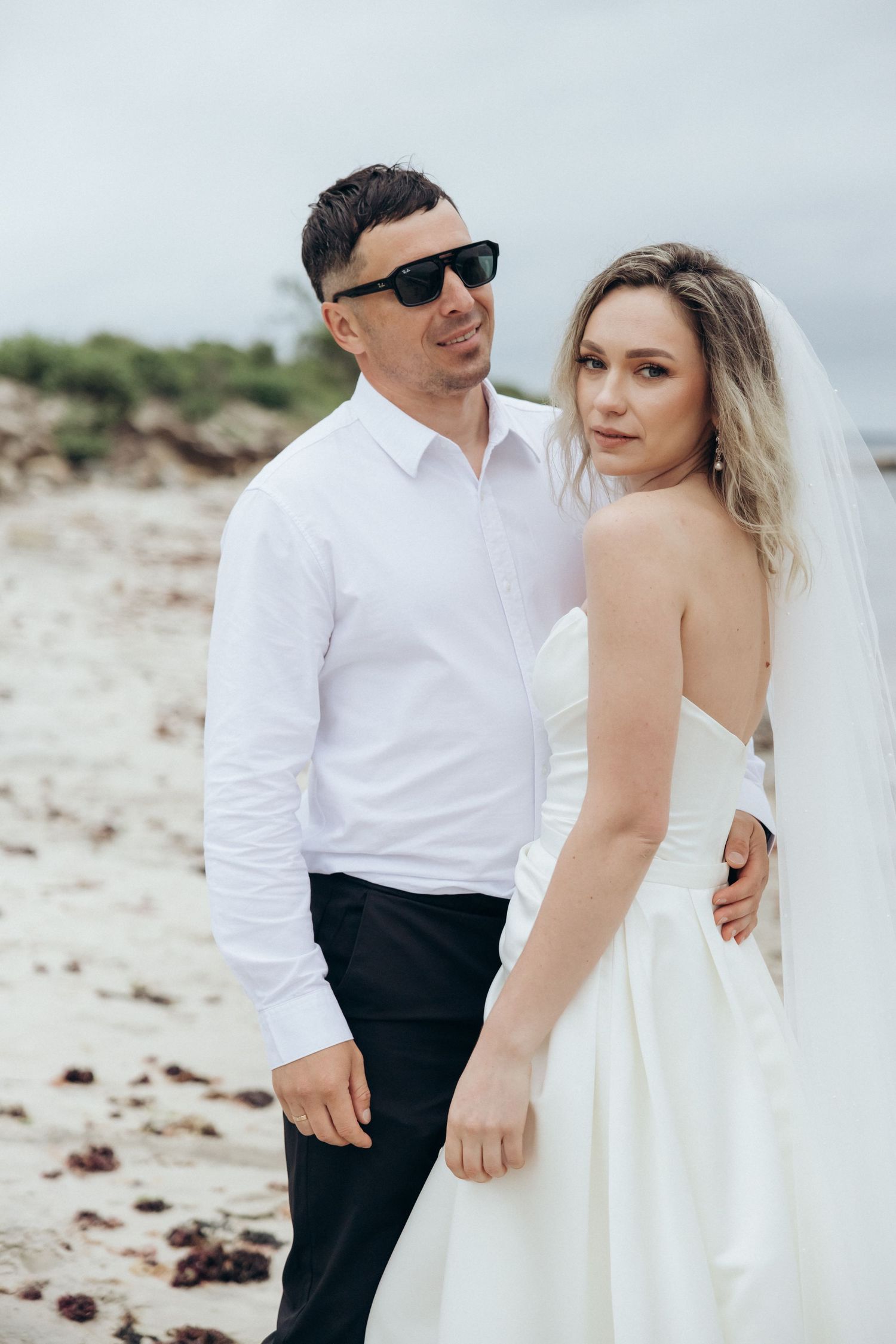 Wedding couple poses together on a scenic beach with rocky shoreline.