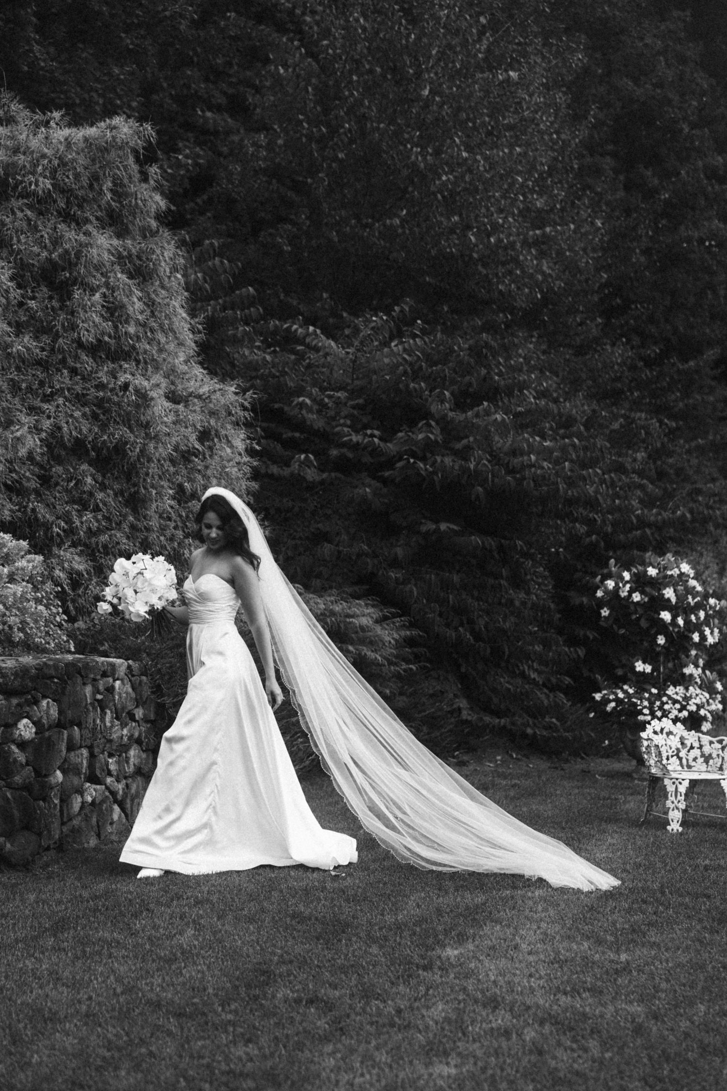 Black and white photo of two wedding dresses creating elegant silhouettes on a garden lawn.