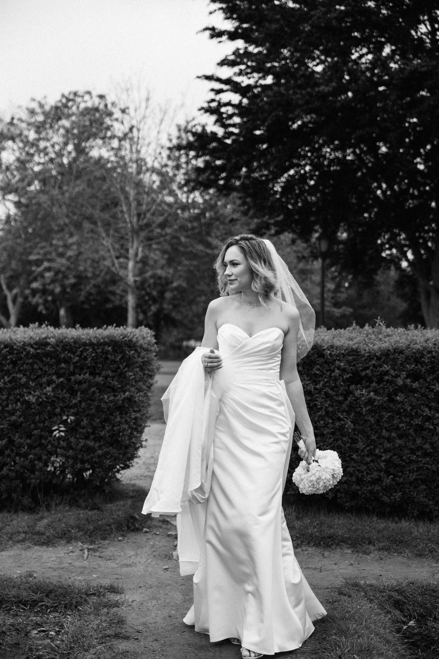 Bride in flowing white dress walking through garden with bouquet.