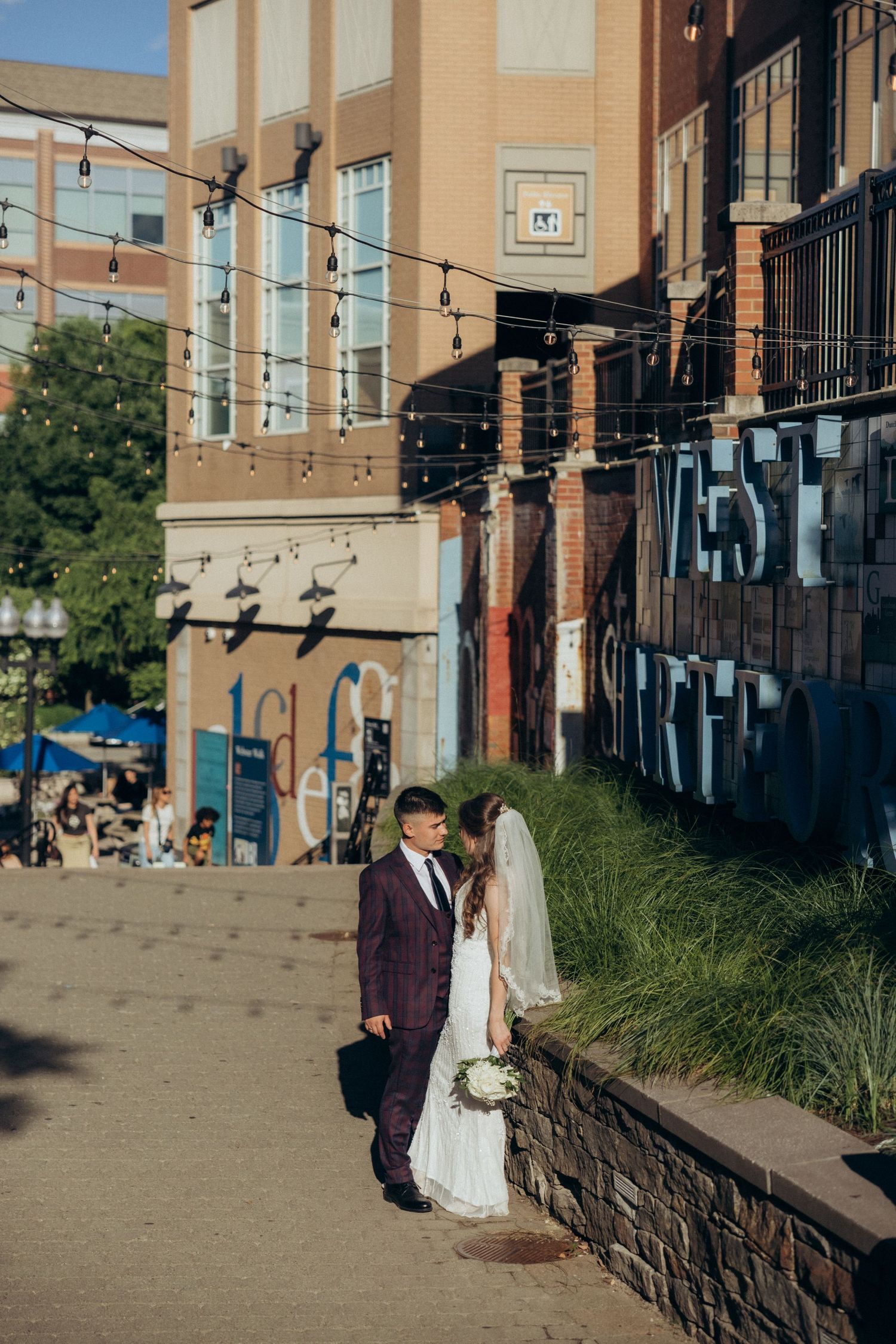 Wedding couple standing near urban brick buildings and landscaping.