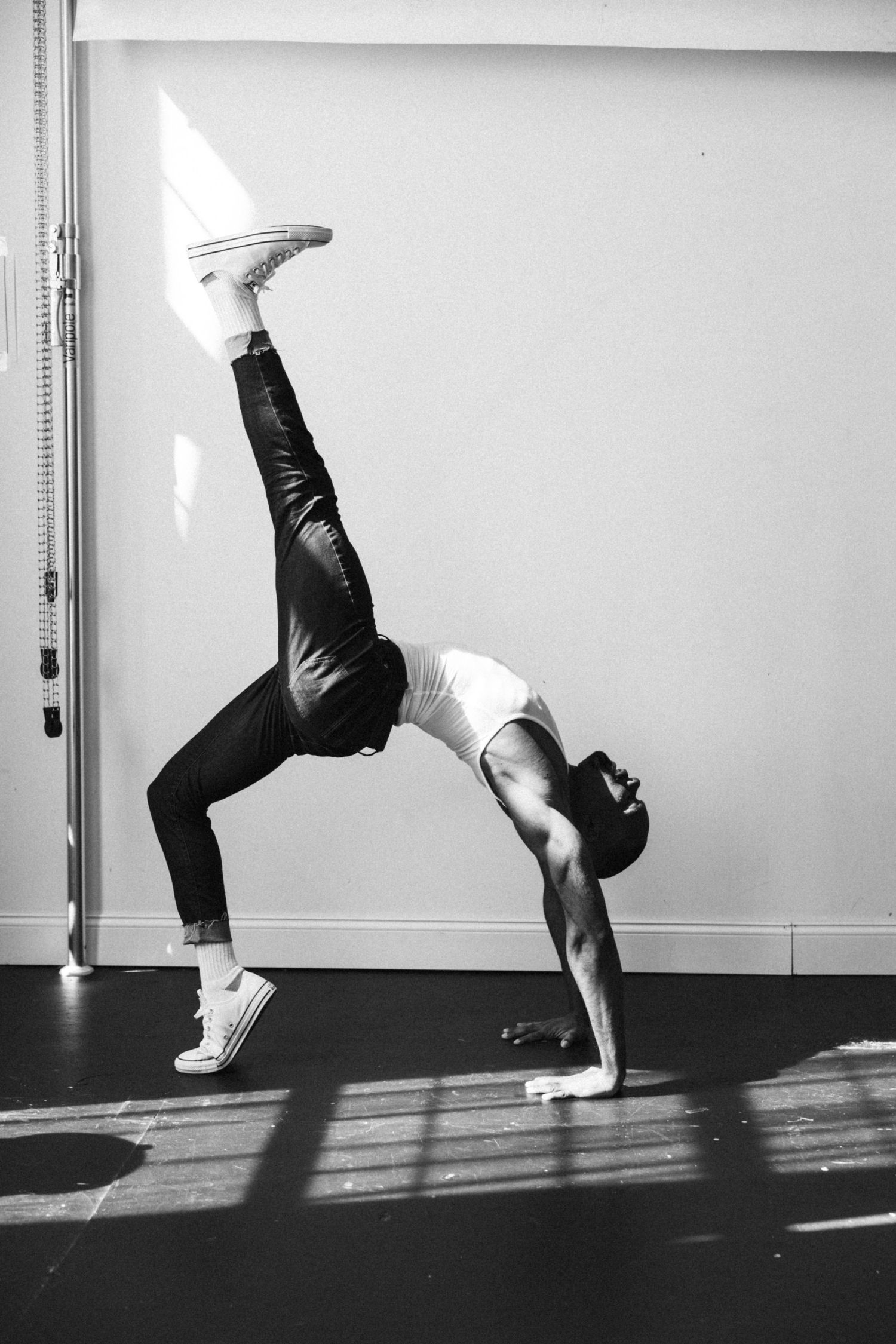 Athletic figure performs impressive backbend bridge pose in black and white workout attire against white wall.