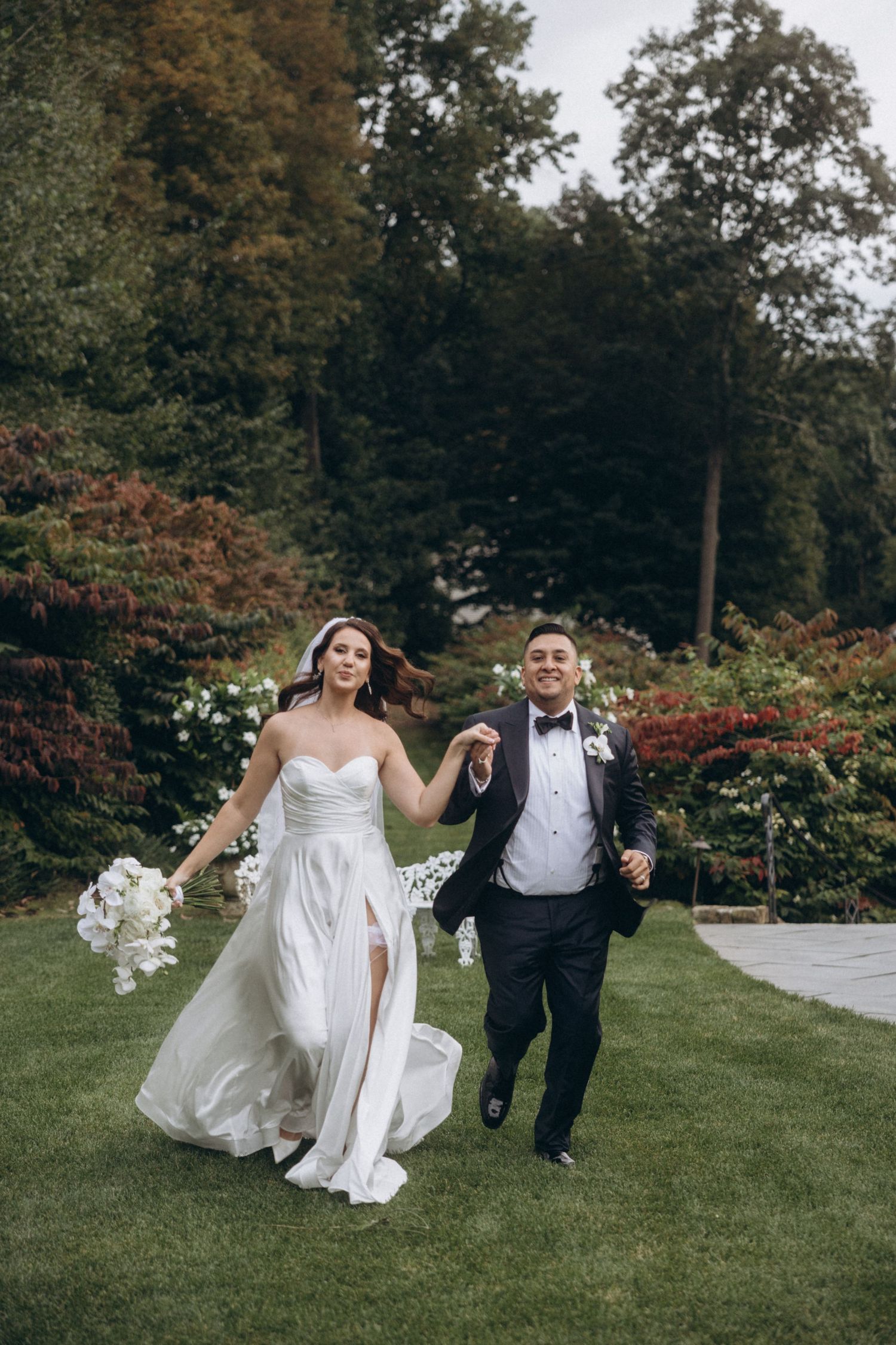 A couple runs playfully through a lush garden setting during their wedding day celebration.