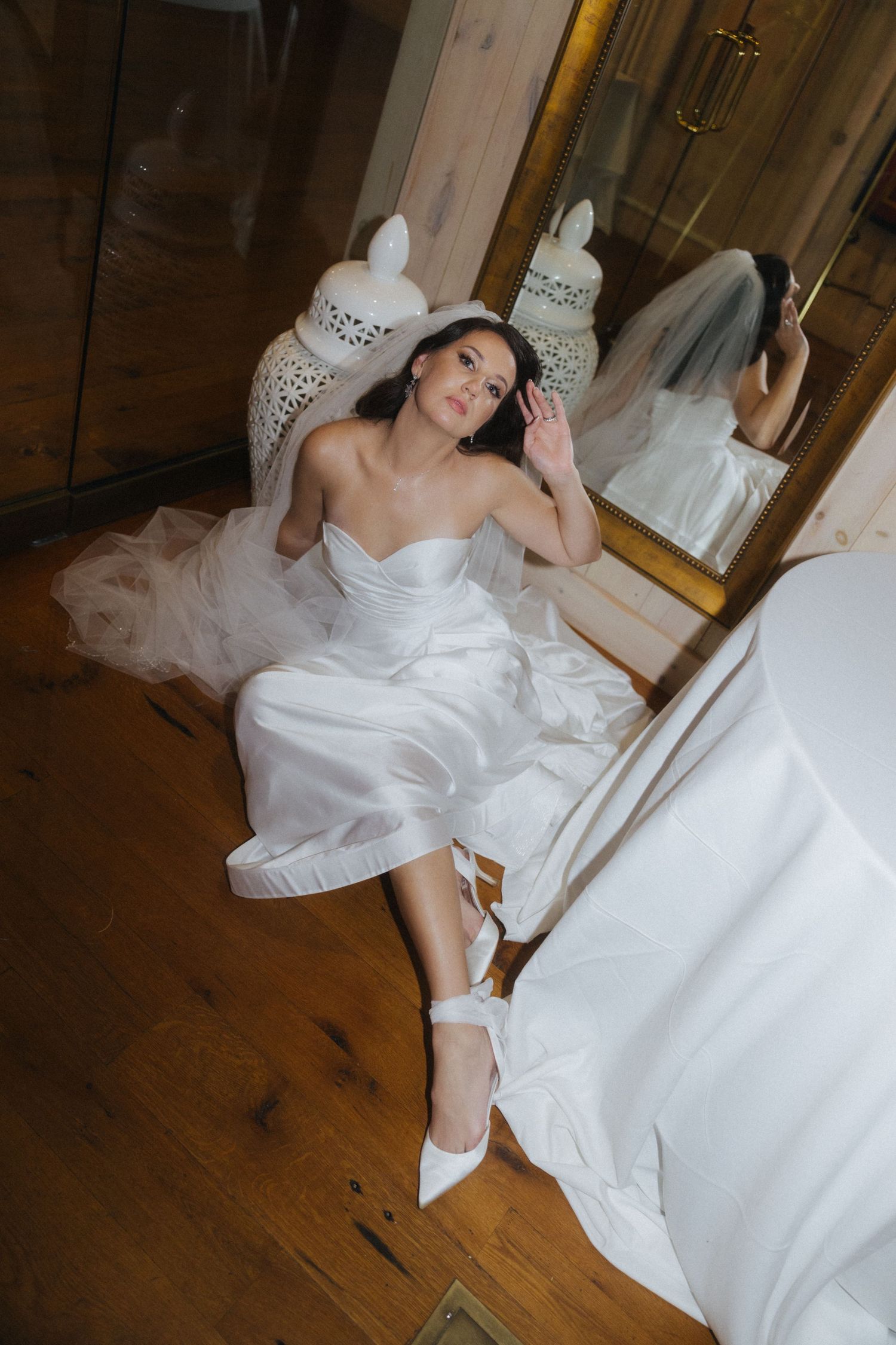 Artistic bridal portrait showing flowing white dress against wooden floor backdrop.