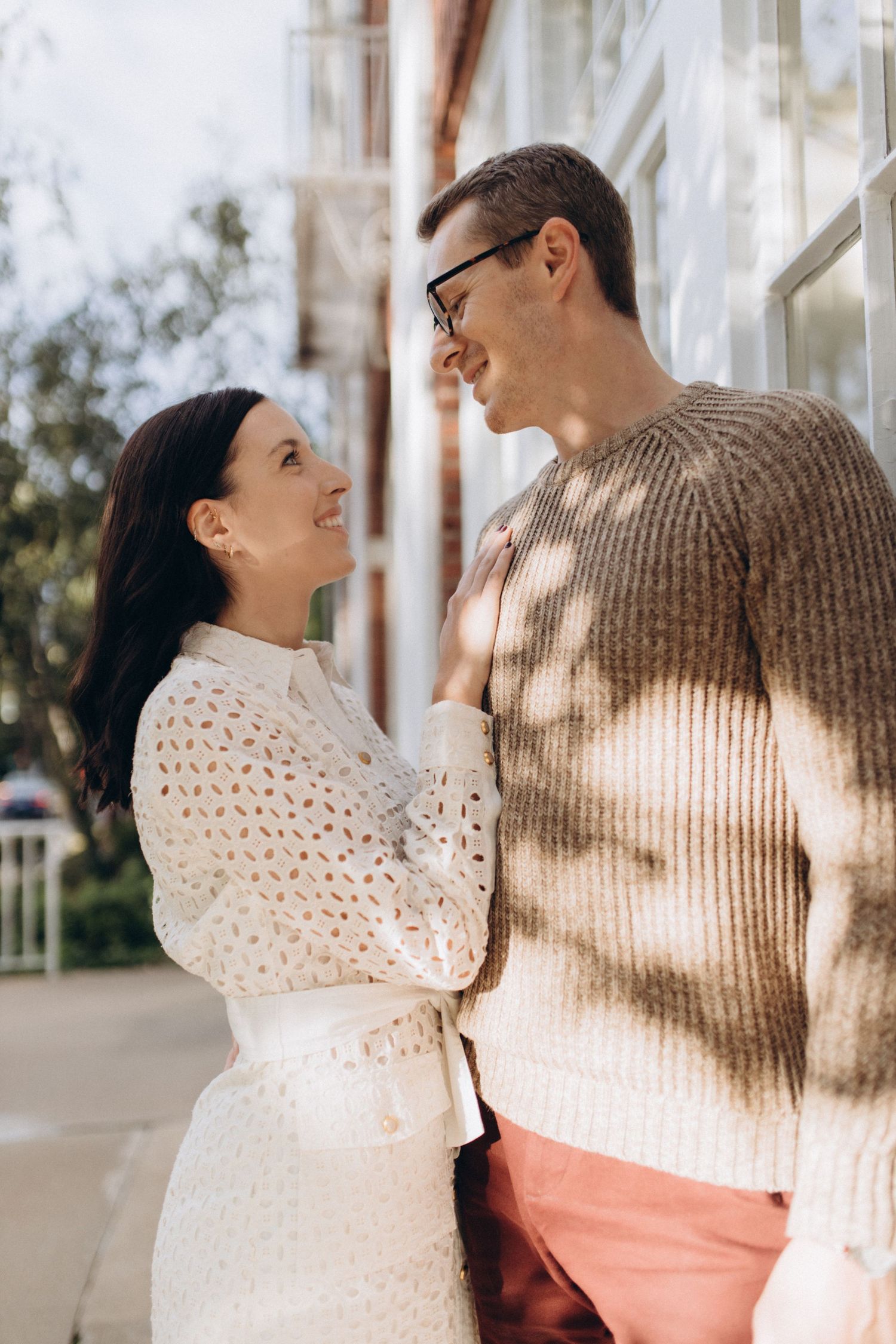 A romantic couple shares a tender moment outdoors, with soft sunlight casting shadows through the trees.