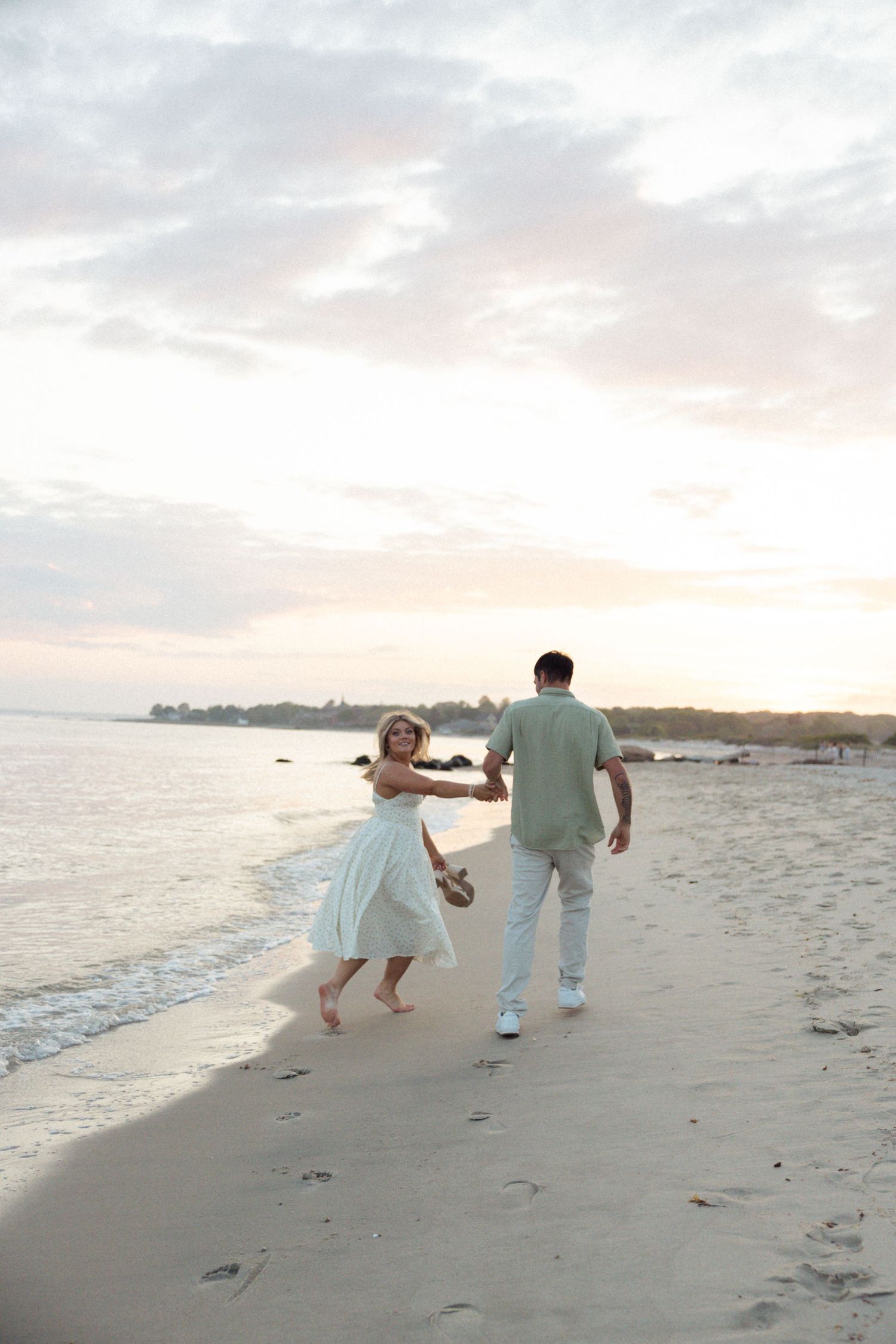 A couple walks hand in hand along a scenic beach at sunset.