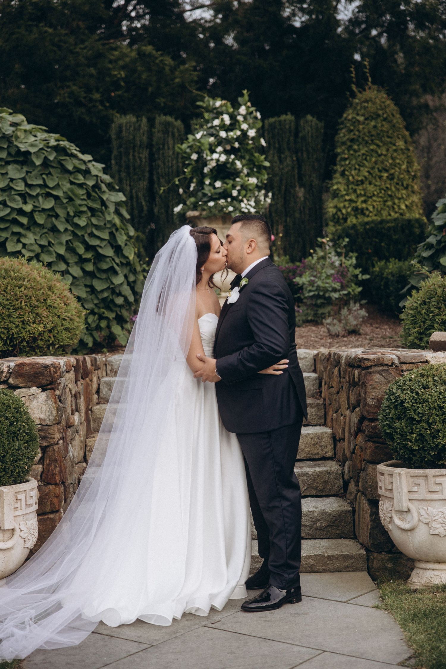 Romantic wedding moment between couple on an elegant stone patio with decorative urns.
