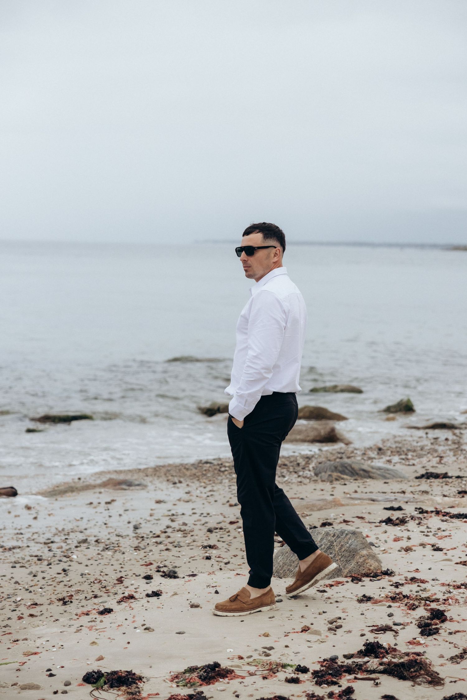 Person in formal wear walking along a rocky beach shoreline.
