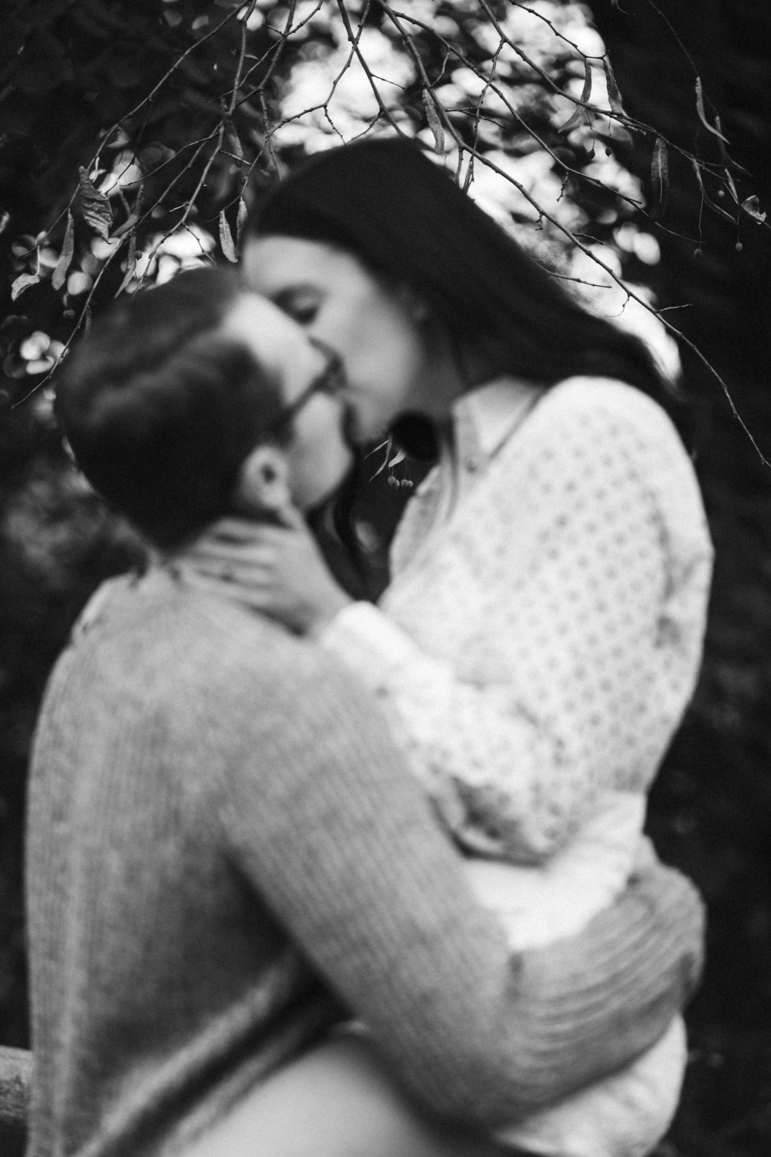 A romantic black and white portrait of an embracing couple beneath dappled light.