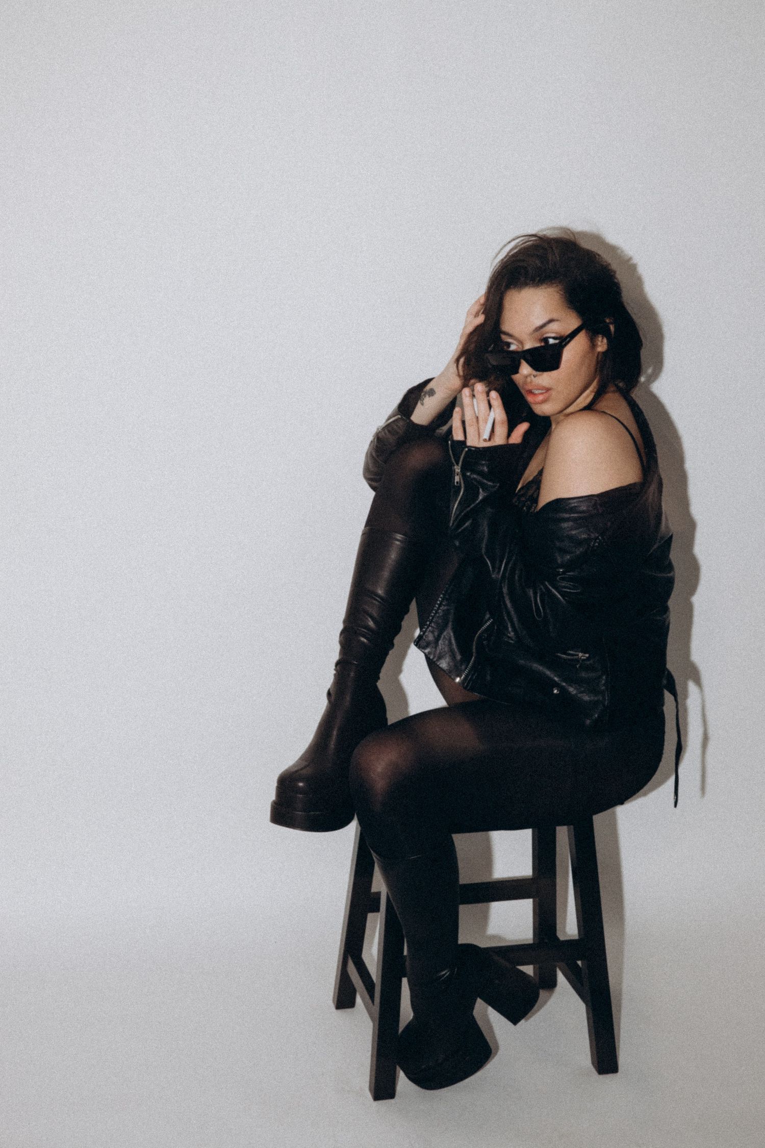 Studio fashion series featuring model in black leather outfit and sunglasses against white background.