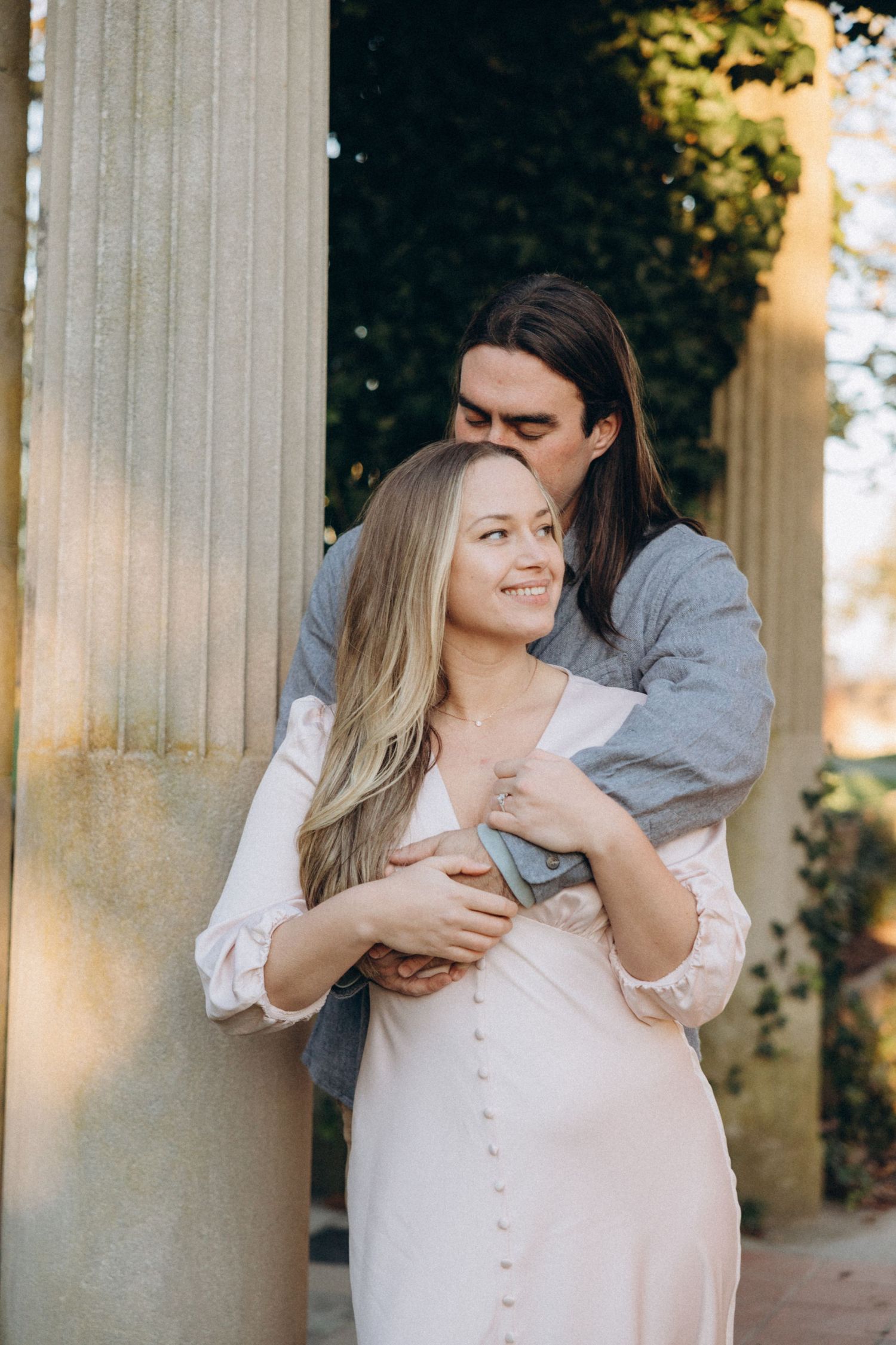 A romantic couple embraces against white columns during an outdoor photoshoot.