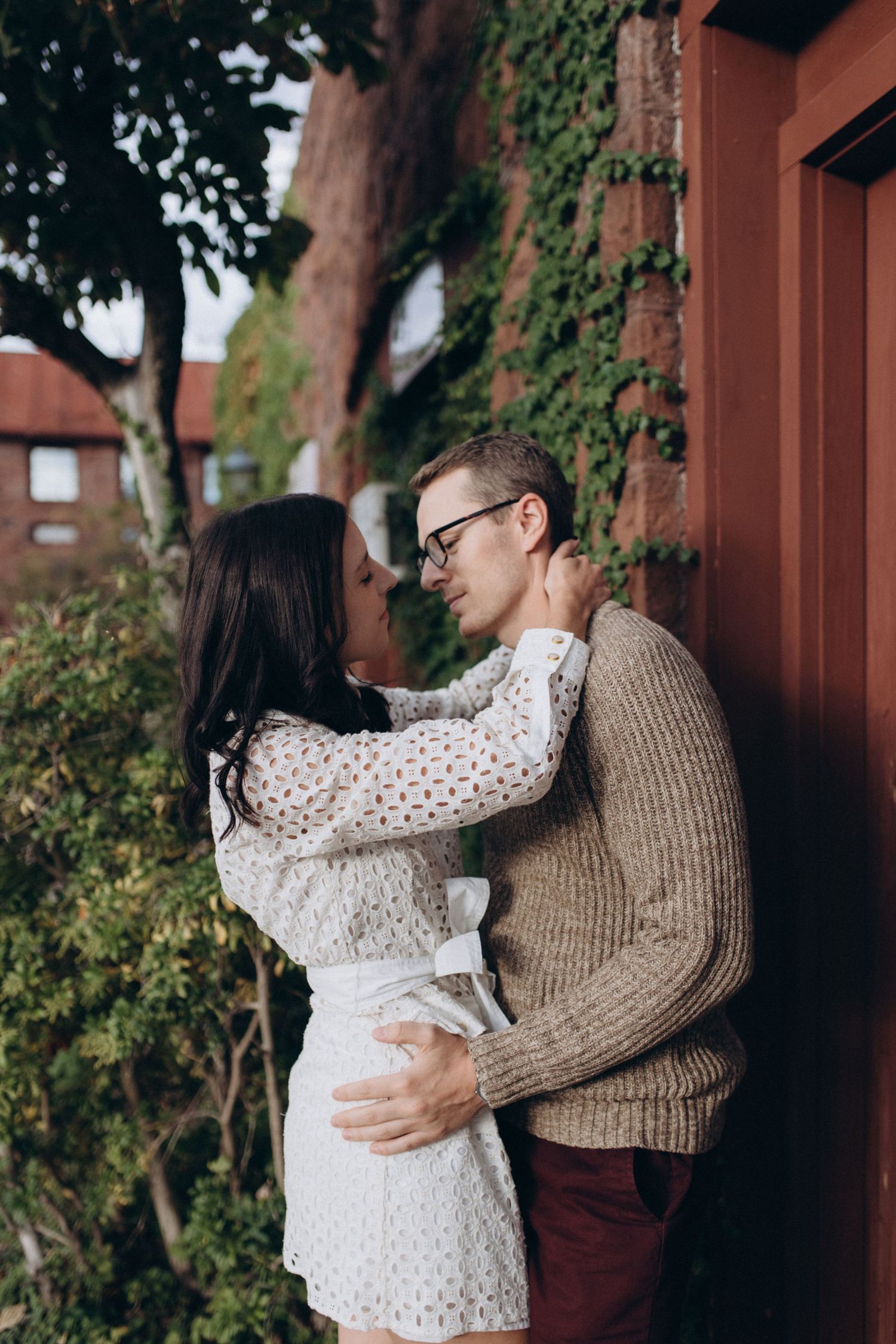 Couple embracing outdoors wearing a white eyelet dress and brown sweater.