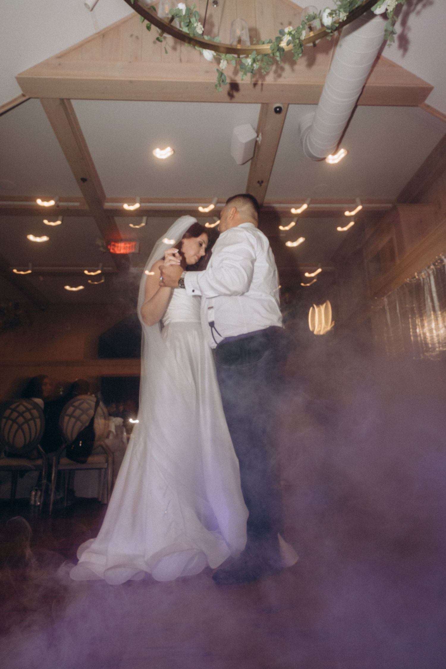First dance captured with dramatic fog effect on illuminated dance floor.