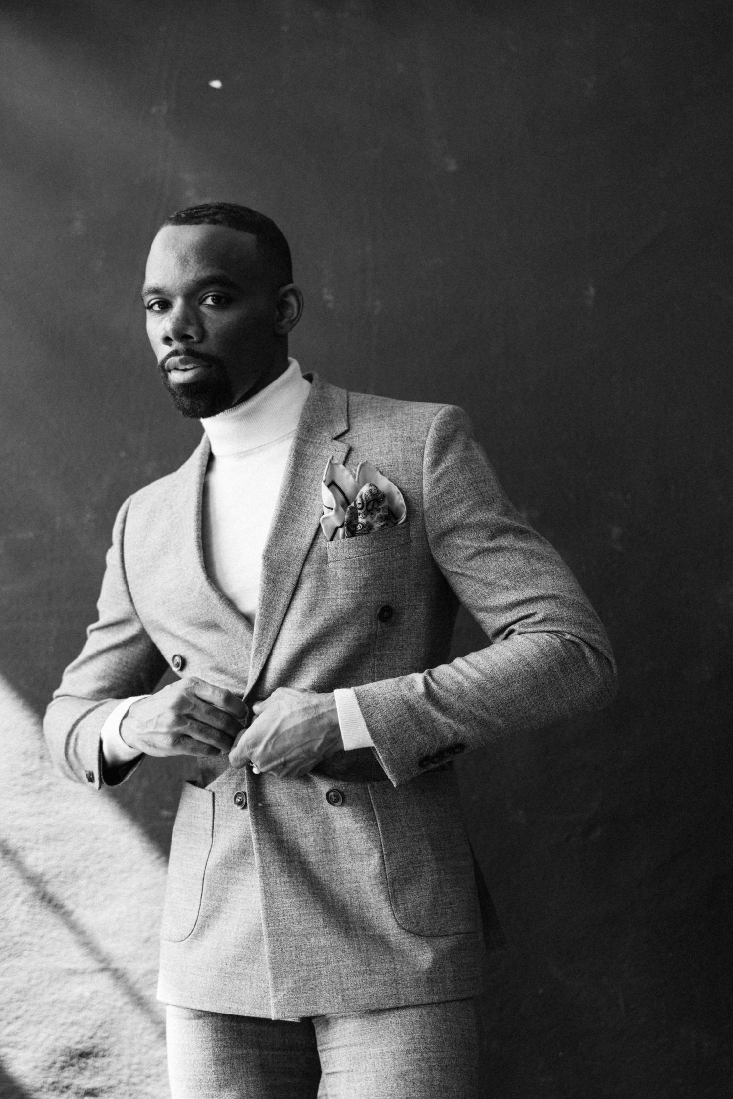 Elegant grey suit with white turtleneck and pocket square captured in black and white.