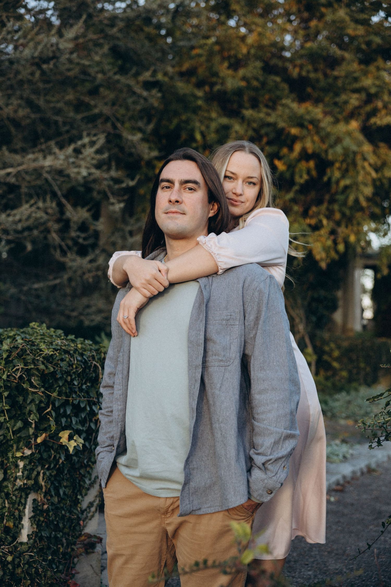 A playful piggyback pose captured outdoors with autumn foliage in the background.
