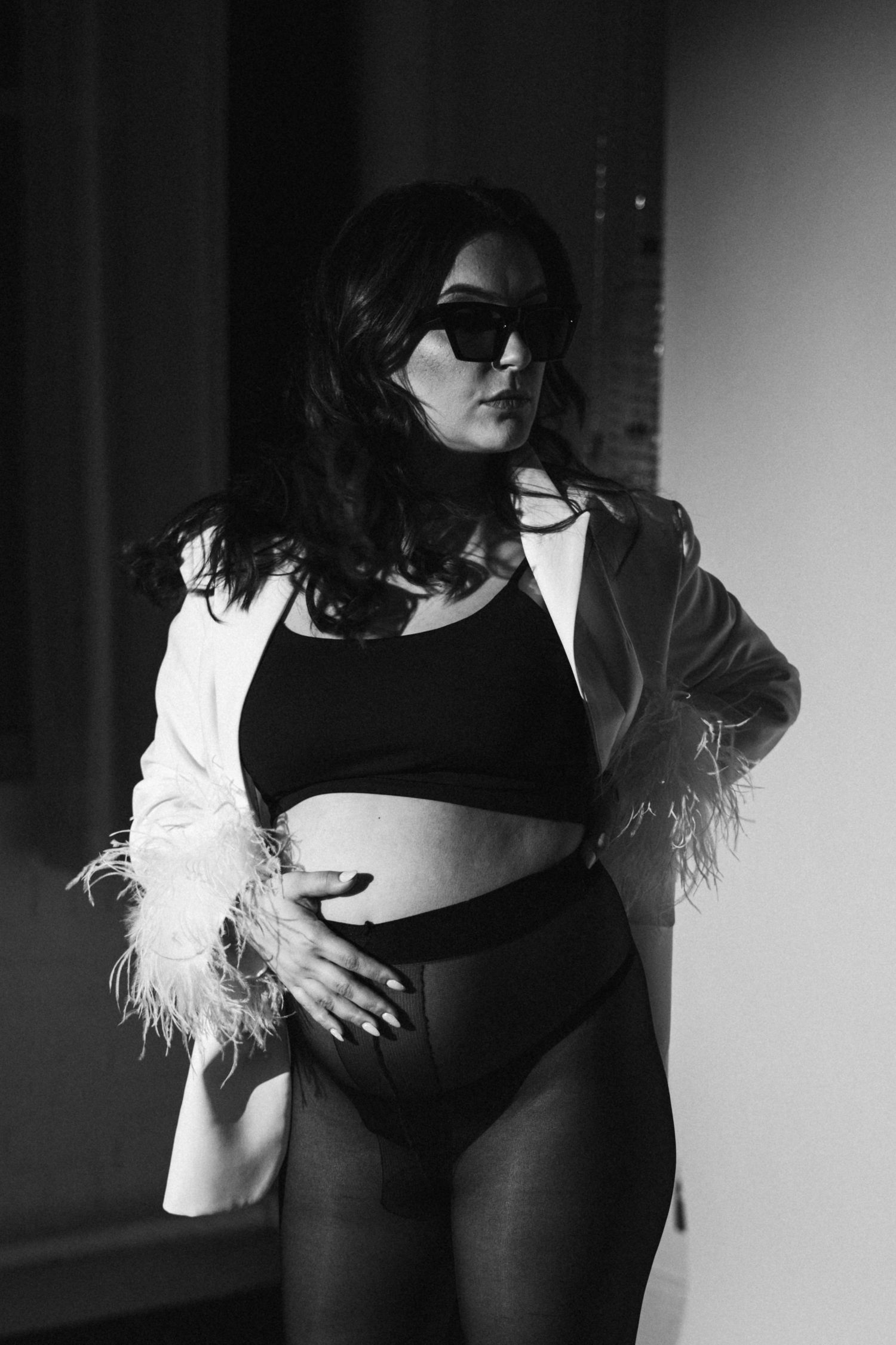 Stylish black and white portrait with sunglasses and white feather-trimmed jacket.