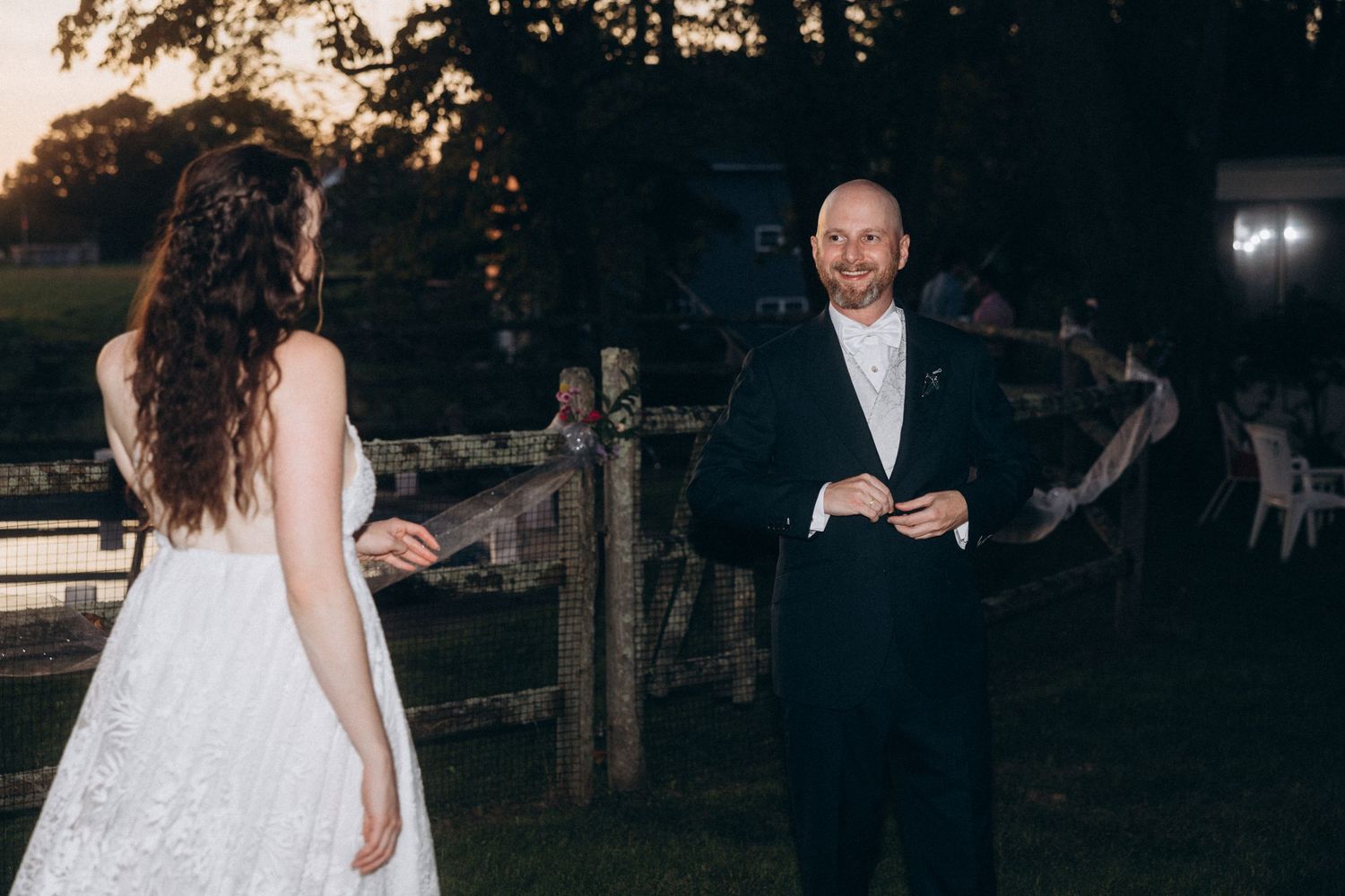 Intimate outdoor wedding moment between couple at sunset near rustic fence.