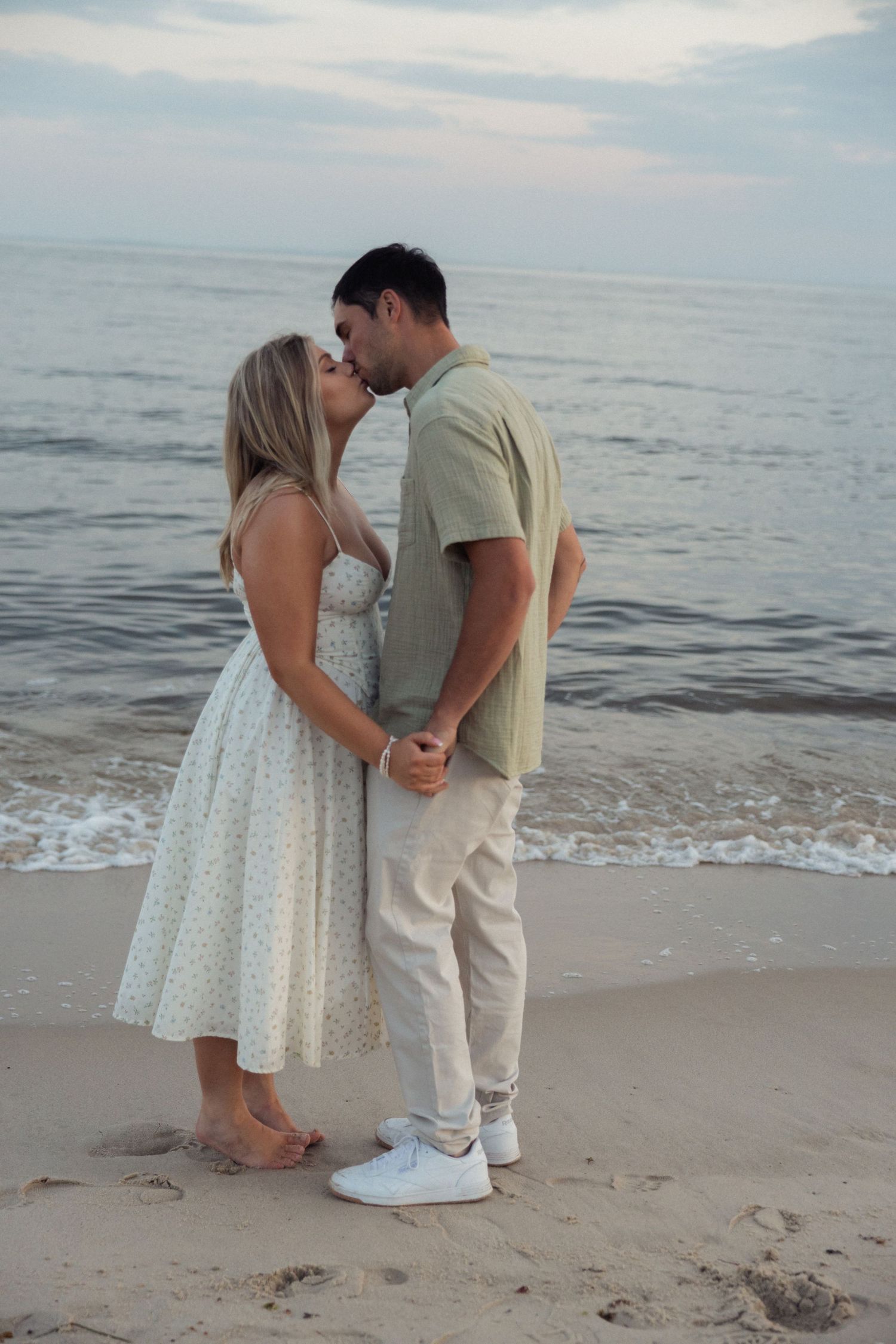 A romantic beach photoshoot featuring a couple in light summer attire near the ocean waves.