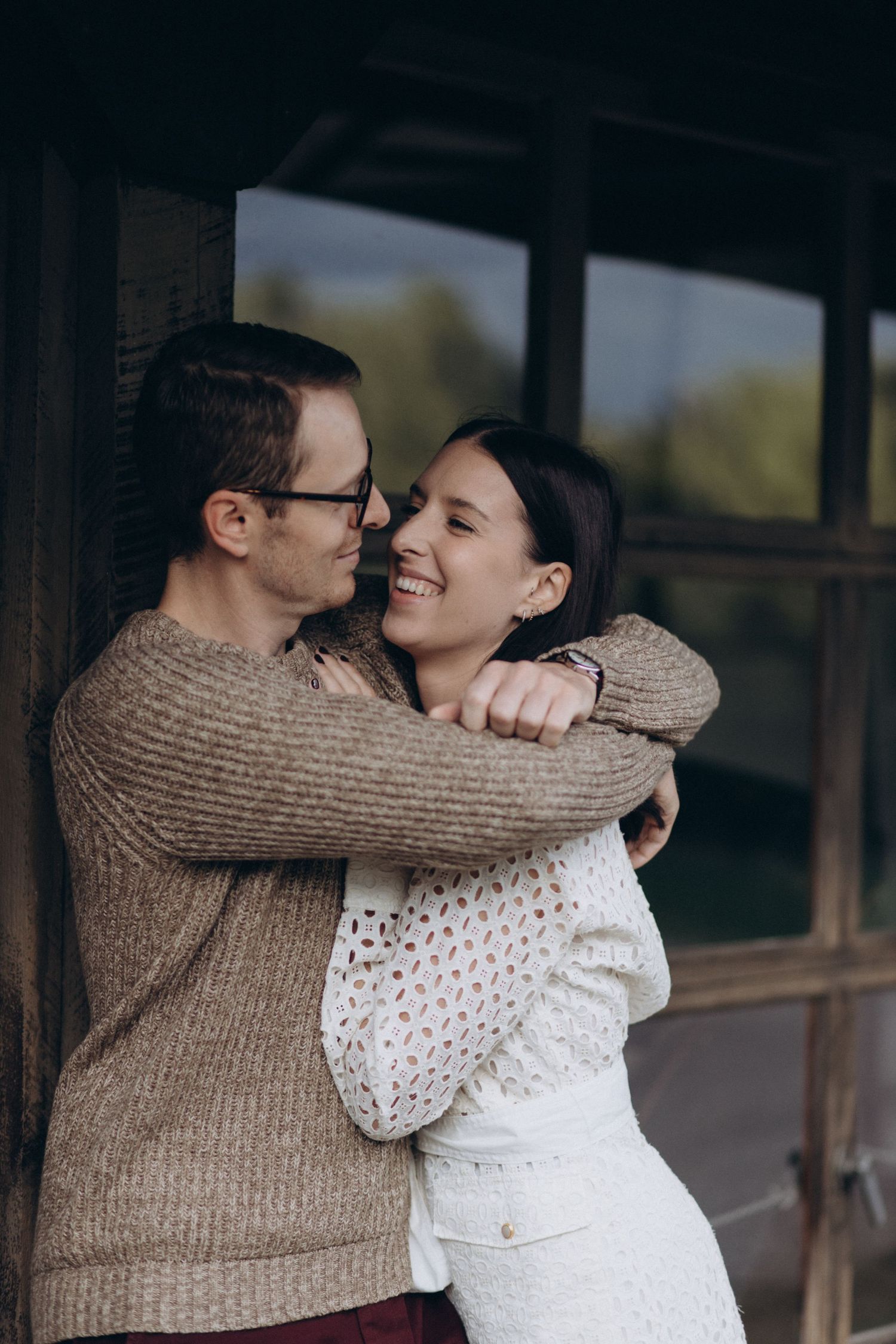An intimate embrace captured in natural lighting against a dark architectural background.