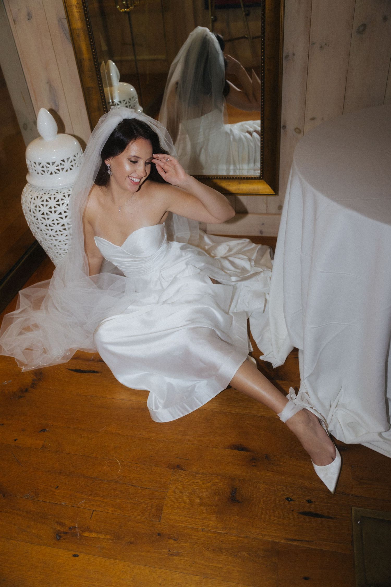 A bride in a white gown poses gracefully on rustic wooden flooring.