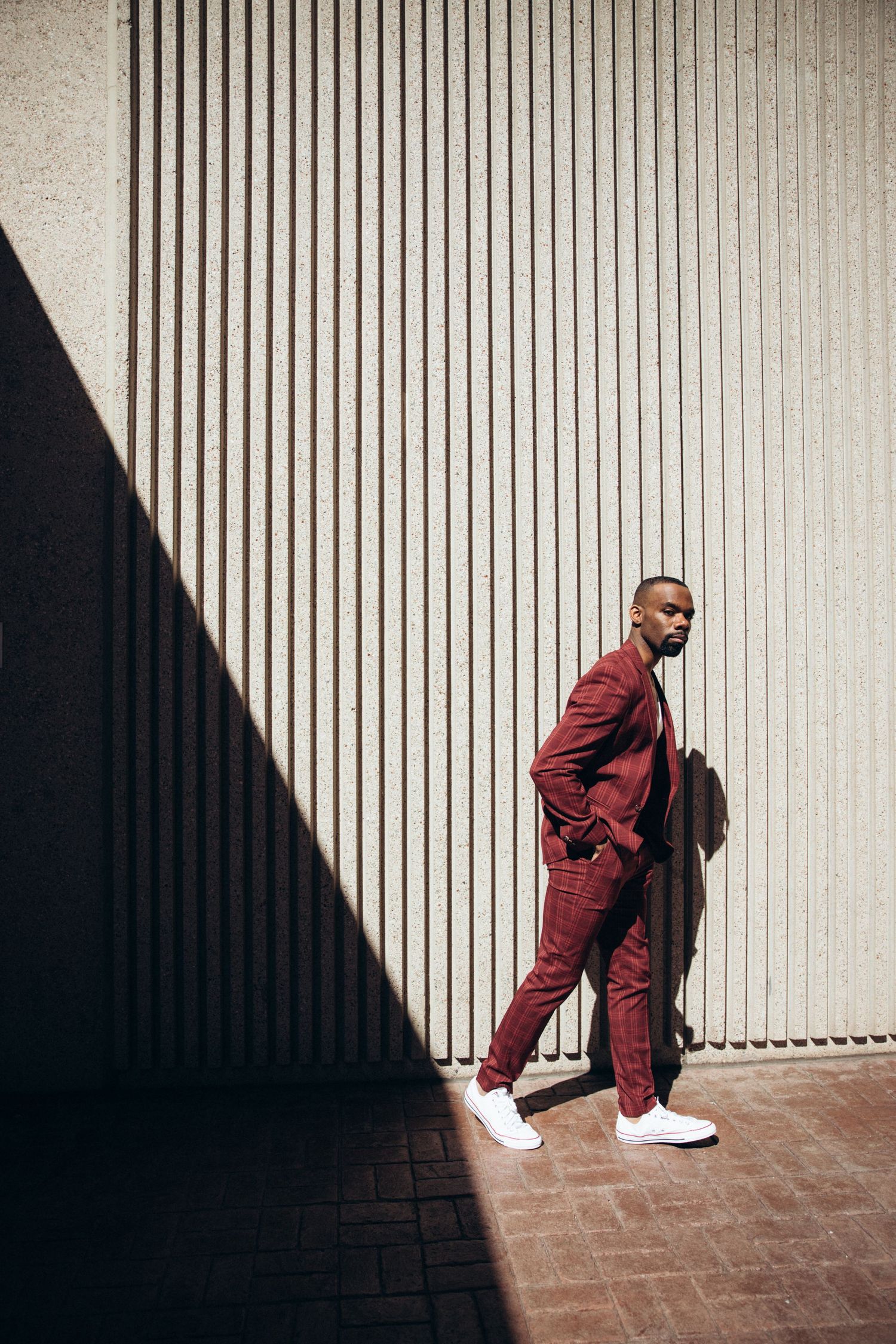 Artistic fashion photoshoot utilizing dramatic shadow play and burgundy attire against white walls.