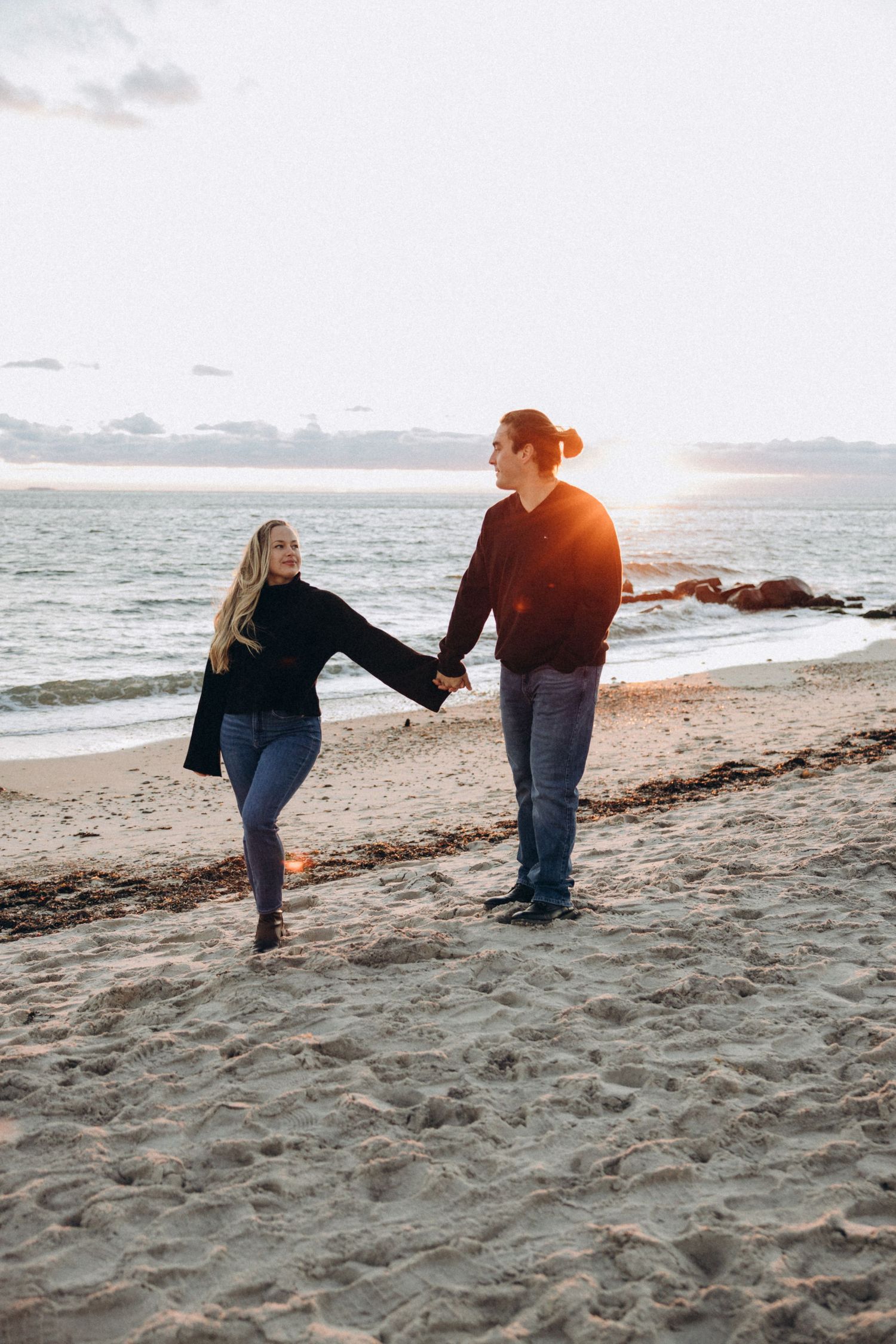 Couple holds hands and plays on the beach during golden hour sunset.