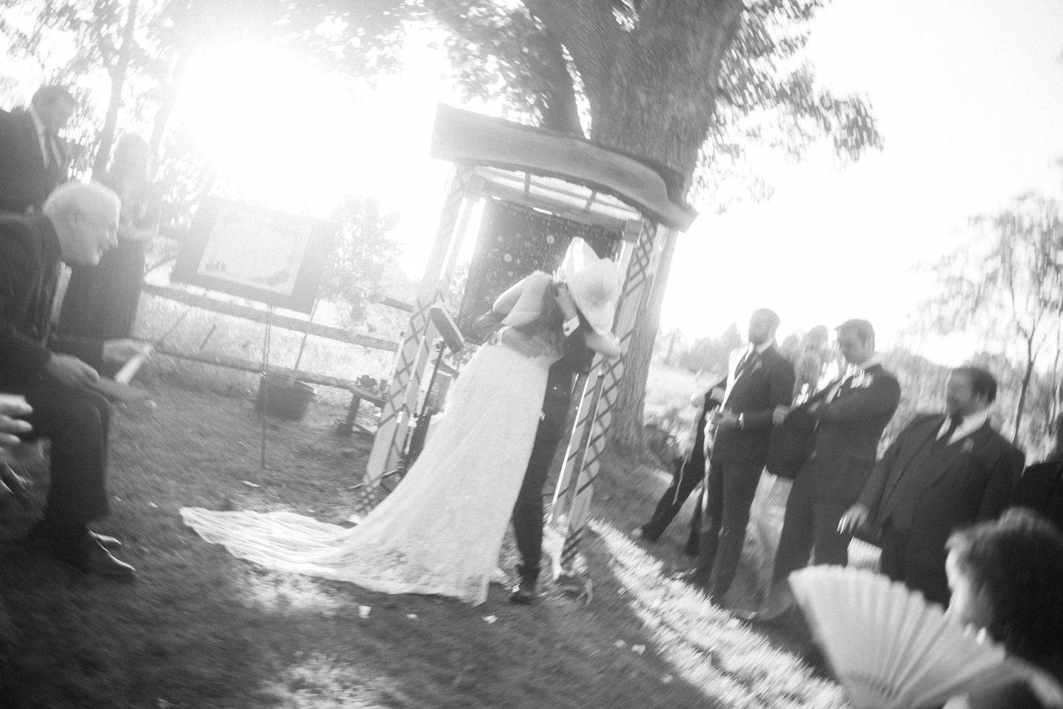 Black and white photo of an outdoor wedding ceremony under a decorated gazebo with guests seated.