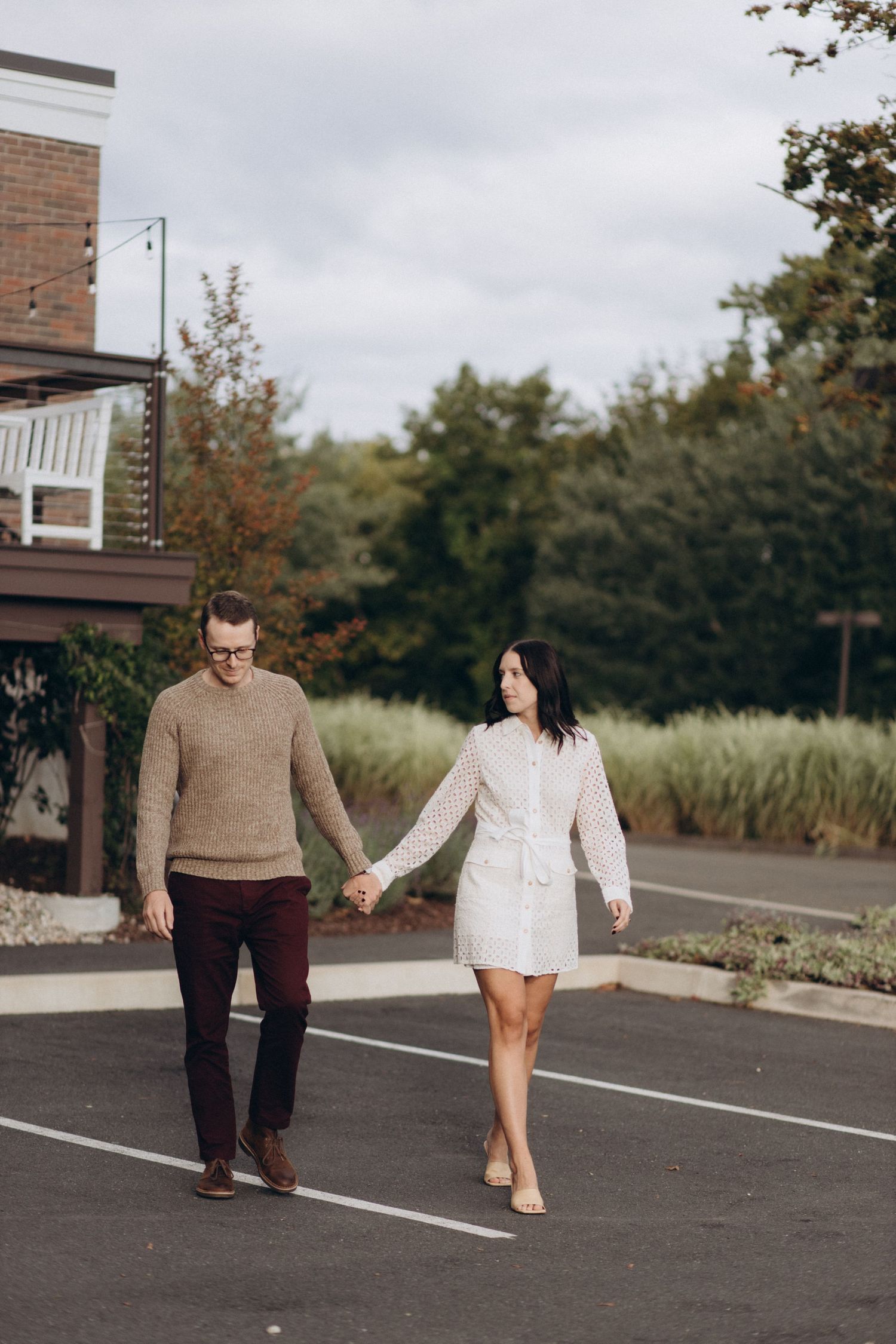Couple holding hands while walking through a parking lot in casual fall attire.