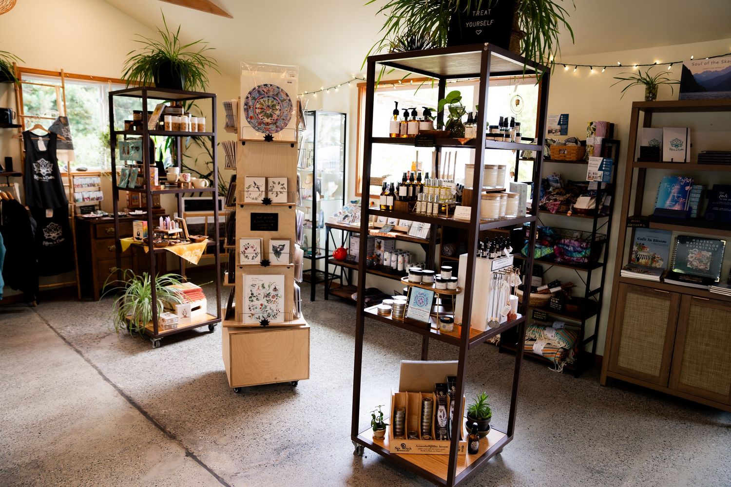 Cozy boutique gift shop interior with metal shelving displaying curated products, plants, and decorative items in a well-lit retail space.