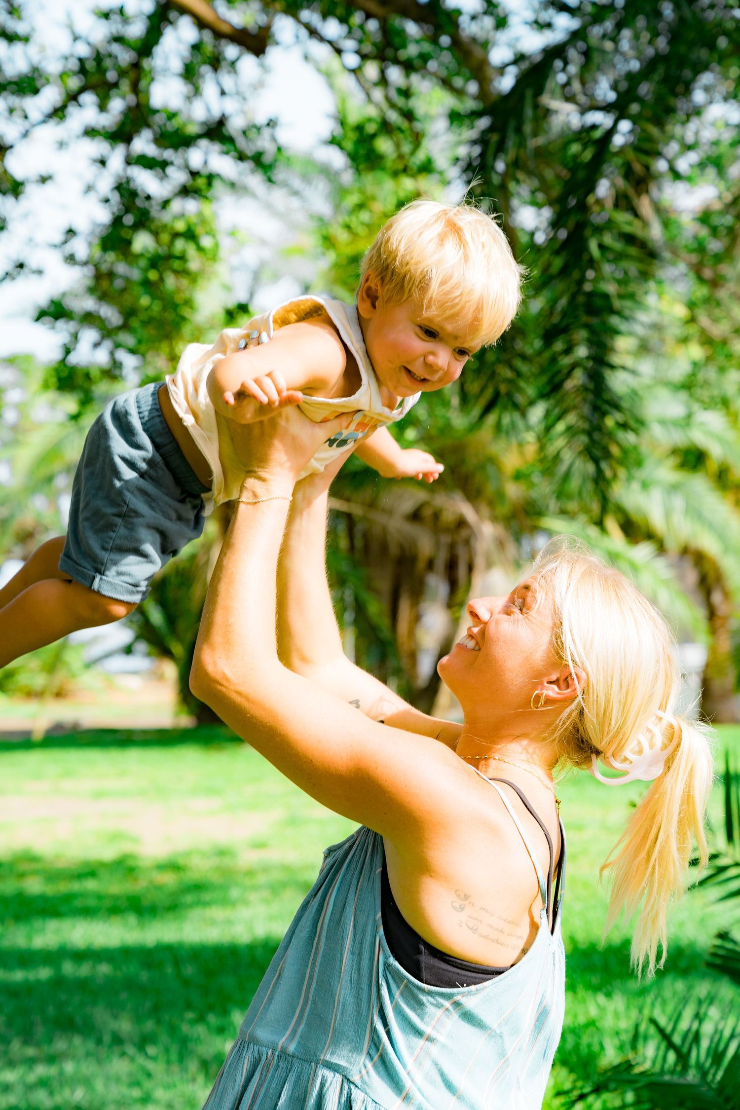 A photo of a blonde mother holding her little boy up in the air and smiling excitedly.