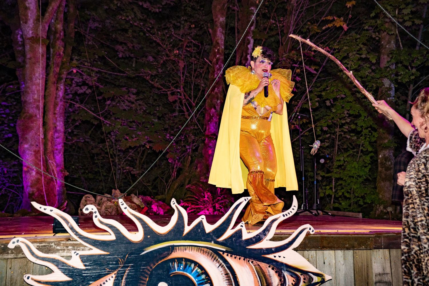 Performer in golden costume stands atop decorated float at colorful outdoor carnival night event.