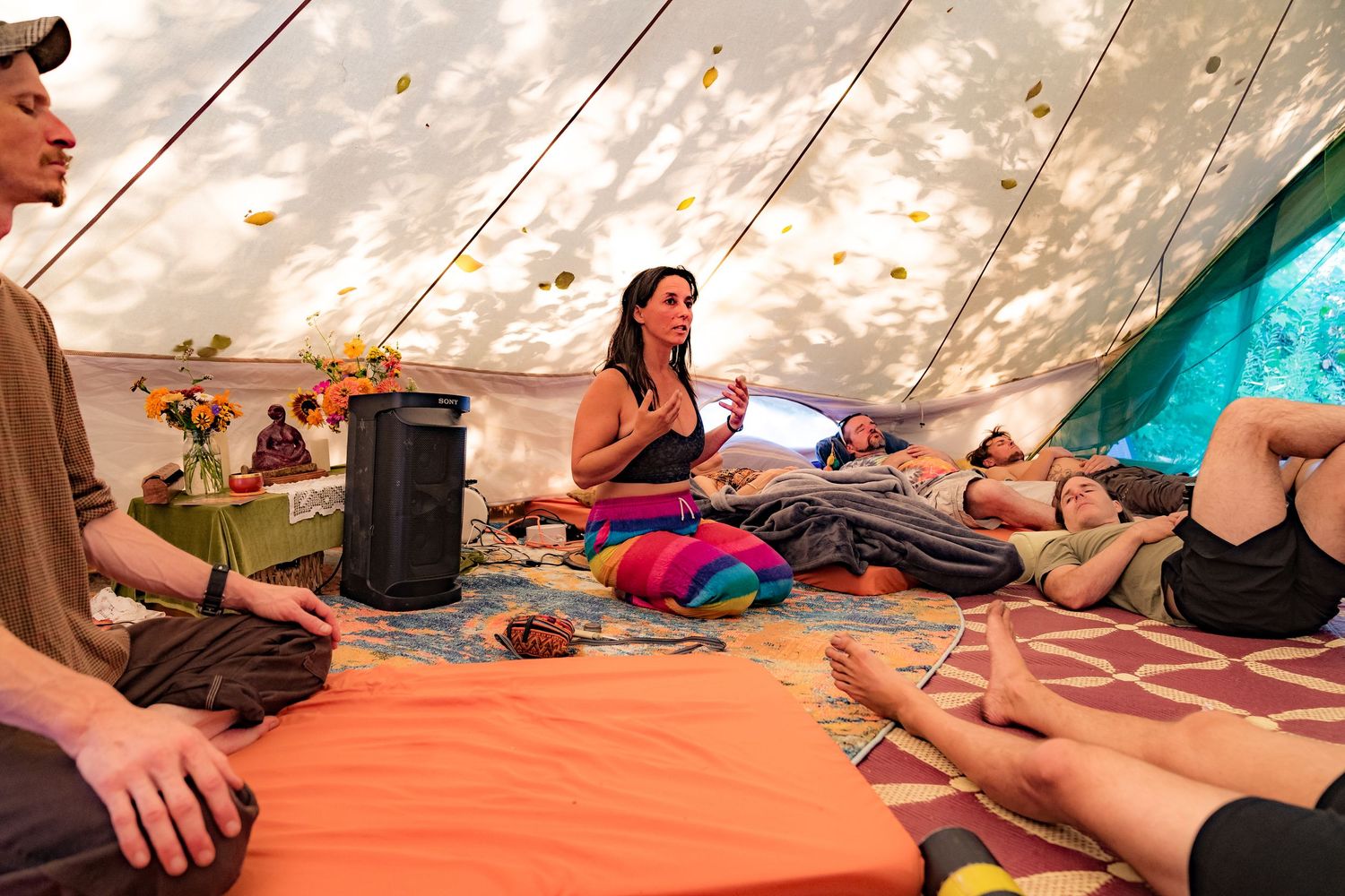 Woman speaking to a group relaxing inside a colorful boho tent at an outdoor festival gathering.