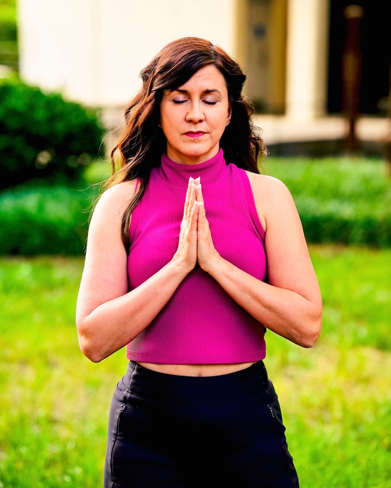 A person in a pink sleeveless top and dark pants performs a series of meditation poses outdoors on a sunny day.