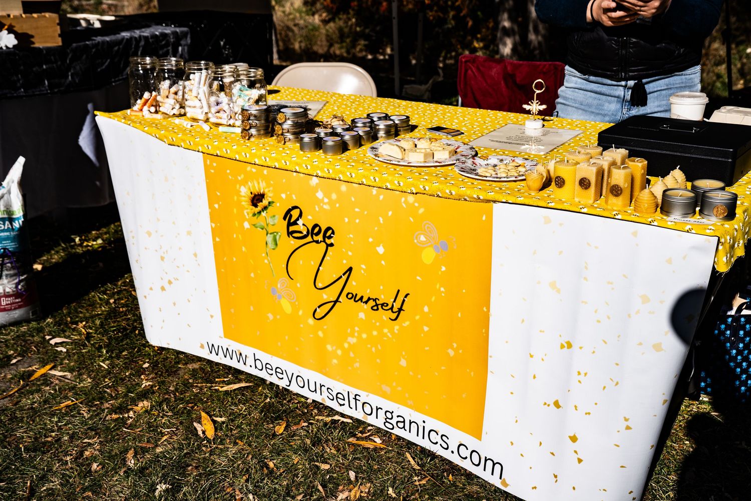 Bee Yourself Honey booth at the farmers market displaying honey jars, candles, and tasting samples.
