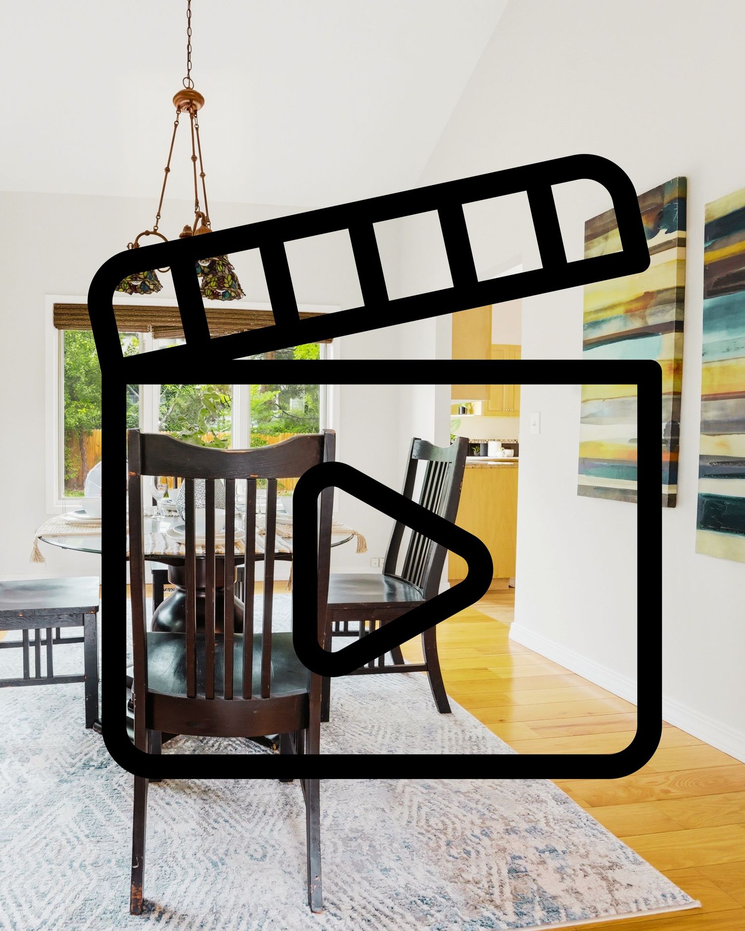 Bright dining room with dark wood chairs, hardwood floors, colorful wall art, and a video play icon overlay.