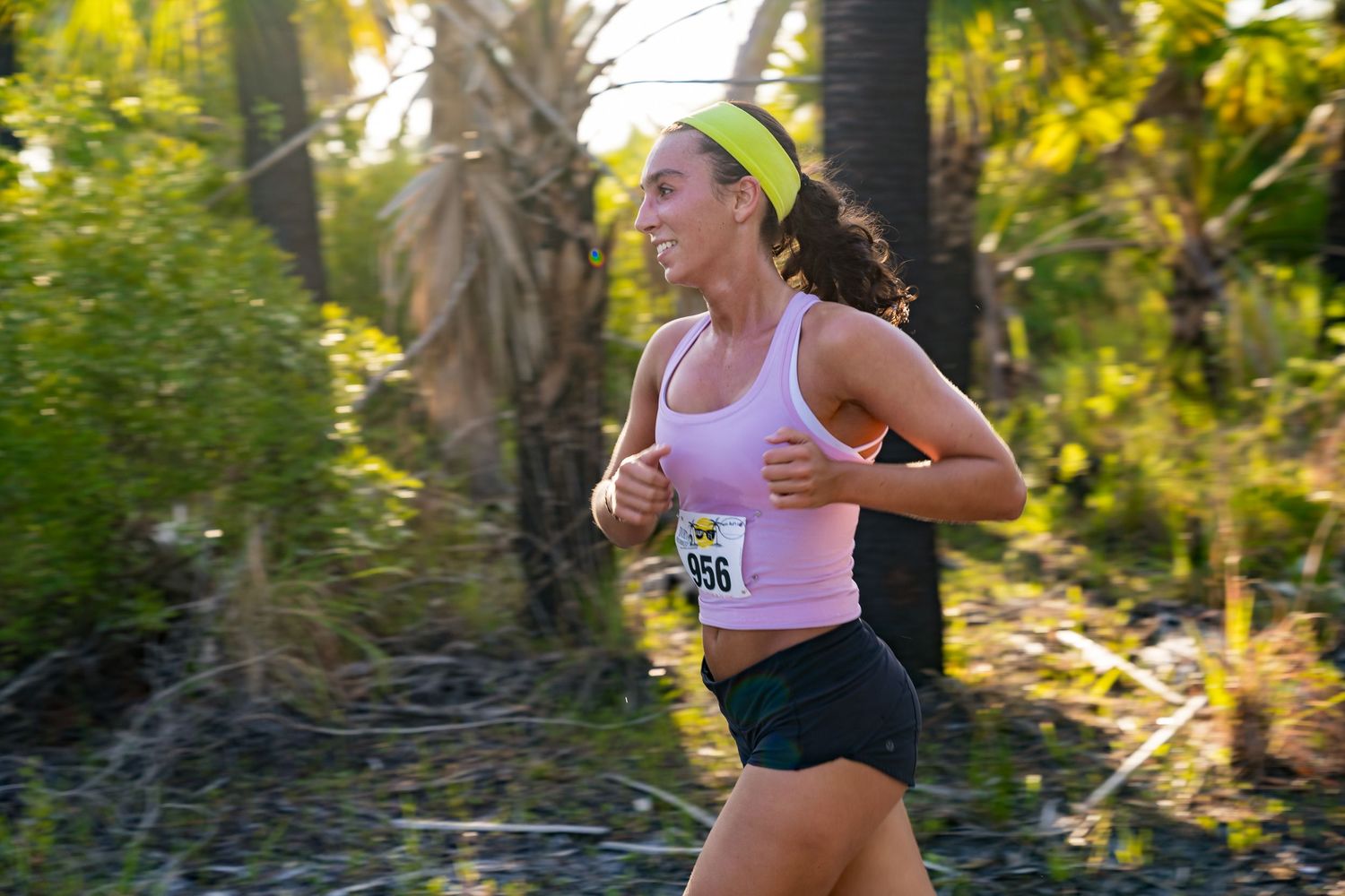 A woman running outdoors wearing a pink tank top.