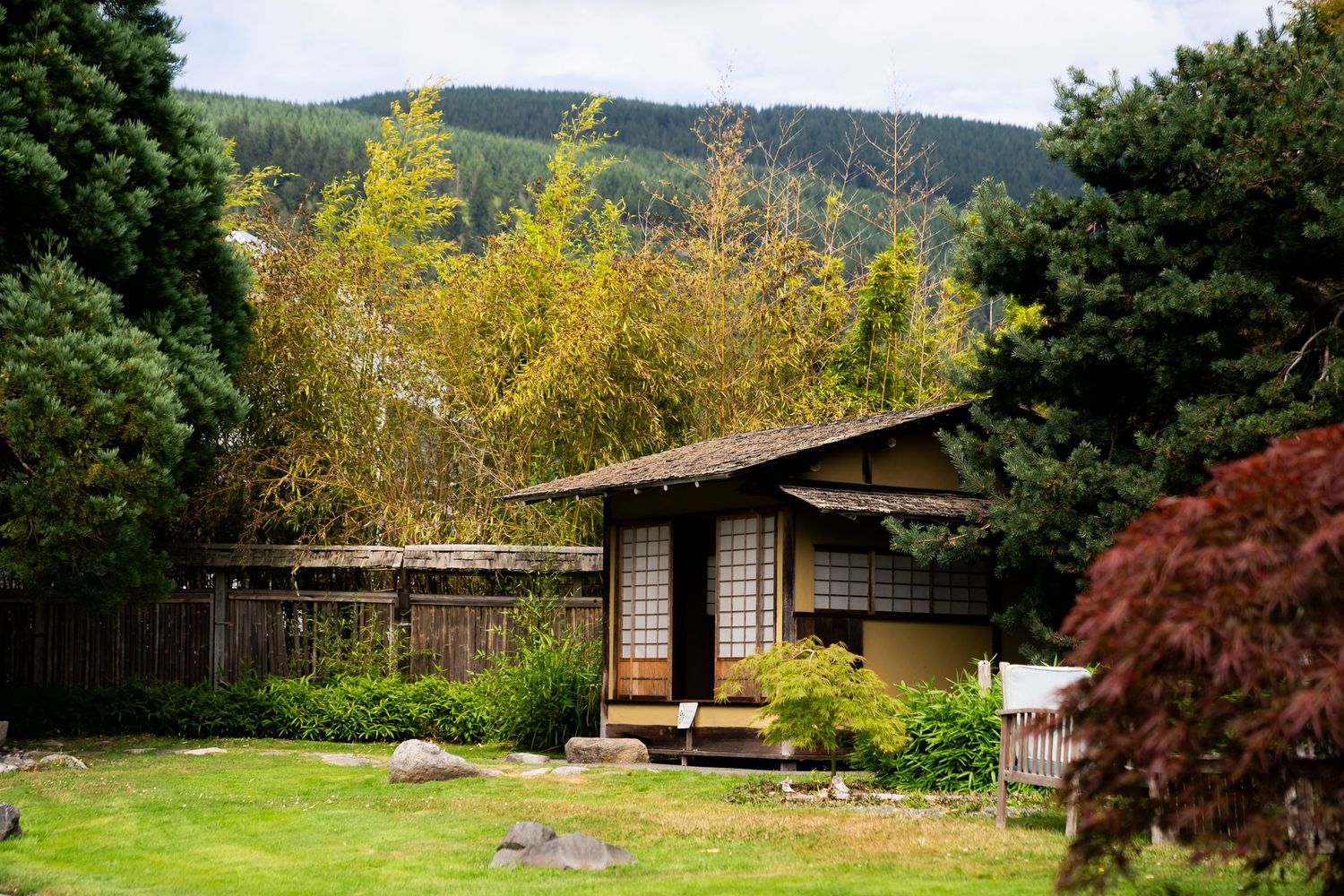 Traditional Japanese tea house surrounded by lush green gardens with forested hills in the background.