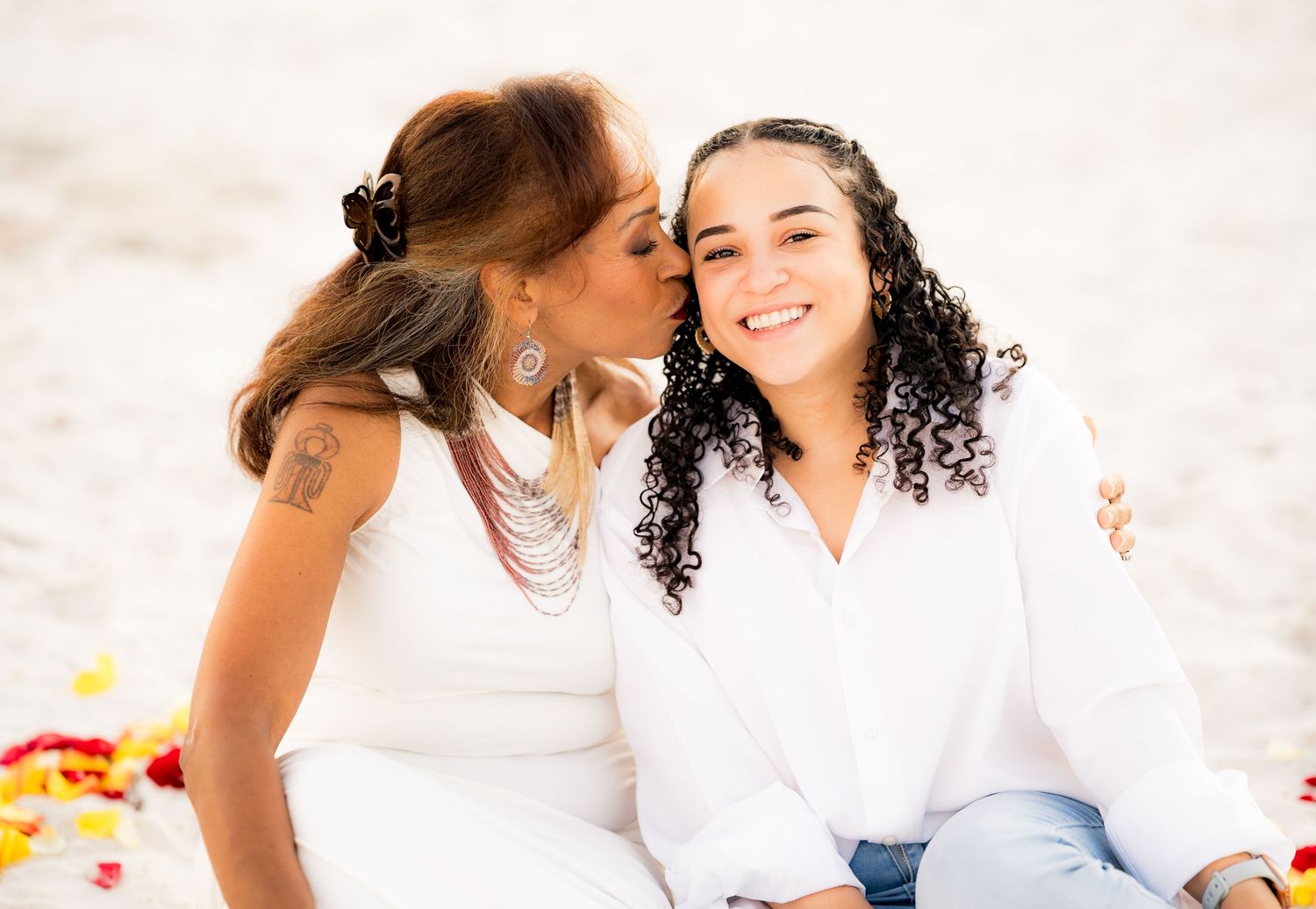Two people share a joyful moment together while sitting outdoors in white clothing.