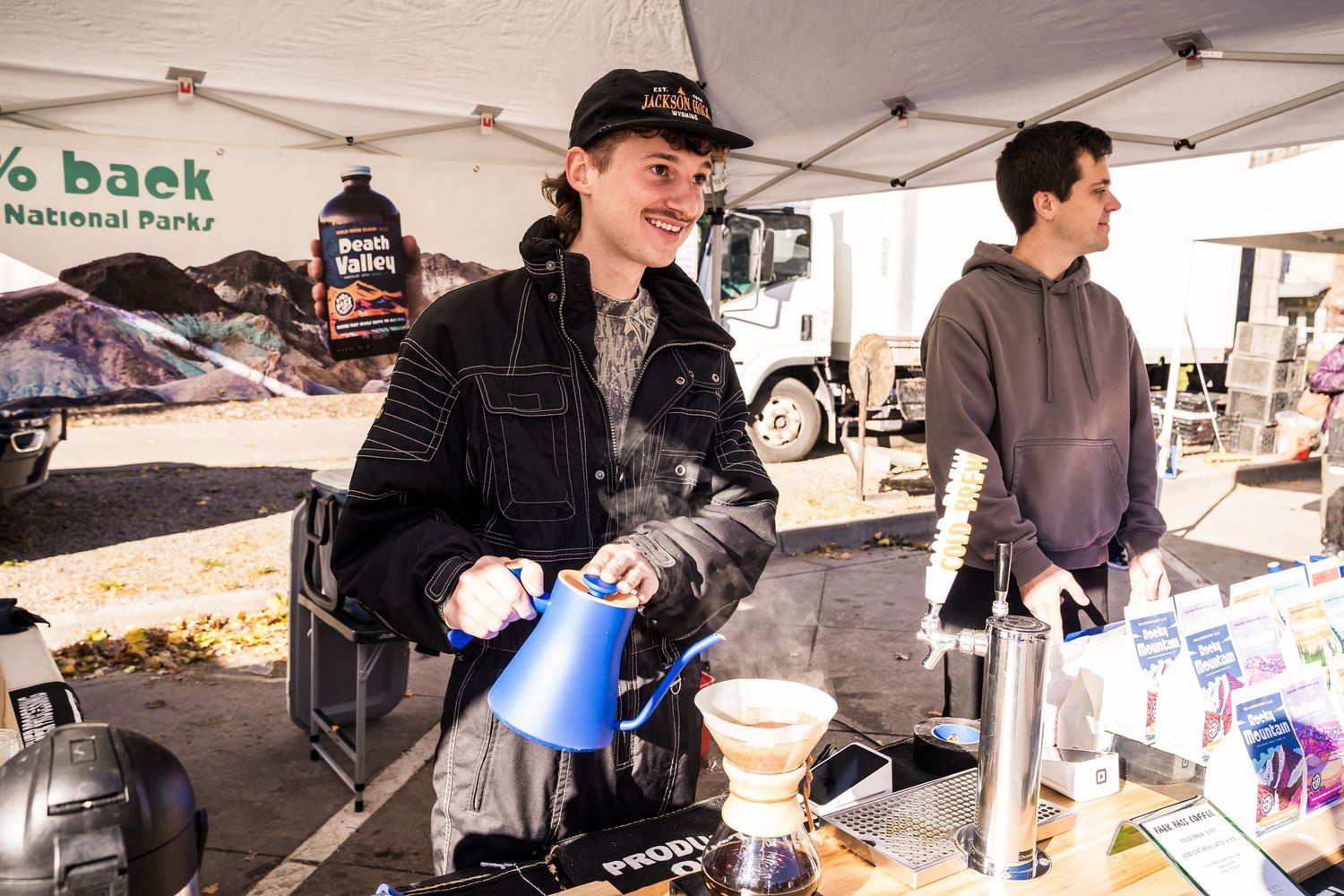 Barista at Park Pass Coffee booth smiling at a customer after pouring freshly brewed coffee at Boulder Farmers Market