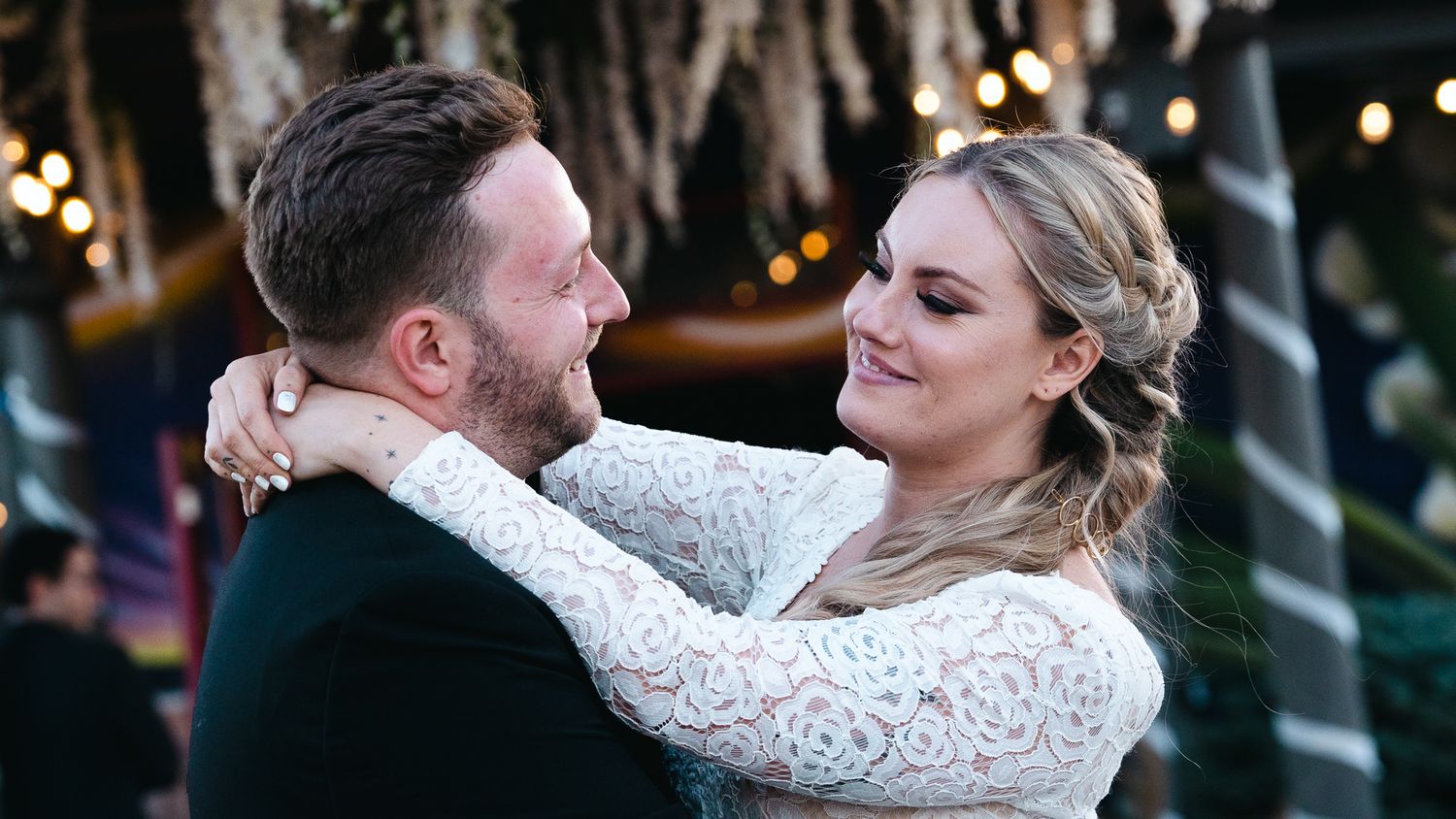 Couple sharing a romantic dance at their wedding reception with warm string lights glowing in the background.
