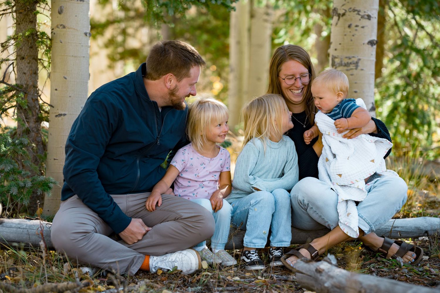 Family sitting together on ground in outdoor setting surrounded by trees and natural light.