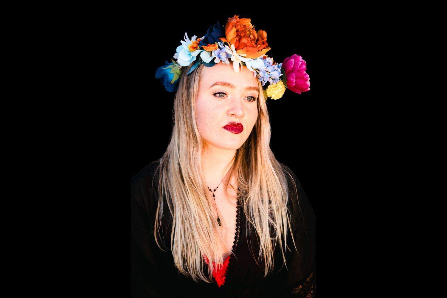 Figure wearing a vibrant floral crown with colorful roses against a black background.