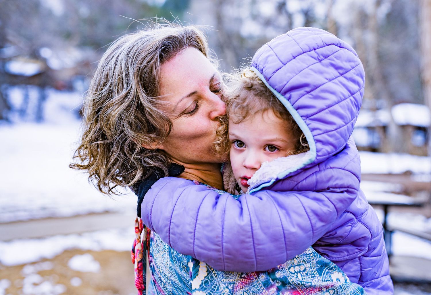 A tender moment captured between parent and child in a snowy winter setting wearing purple outerwear.