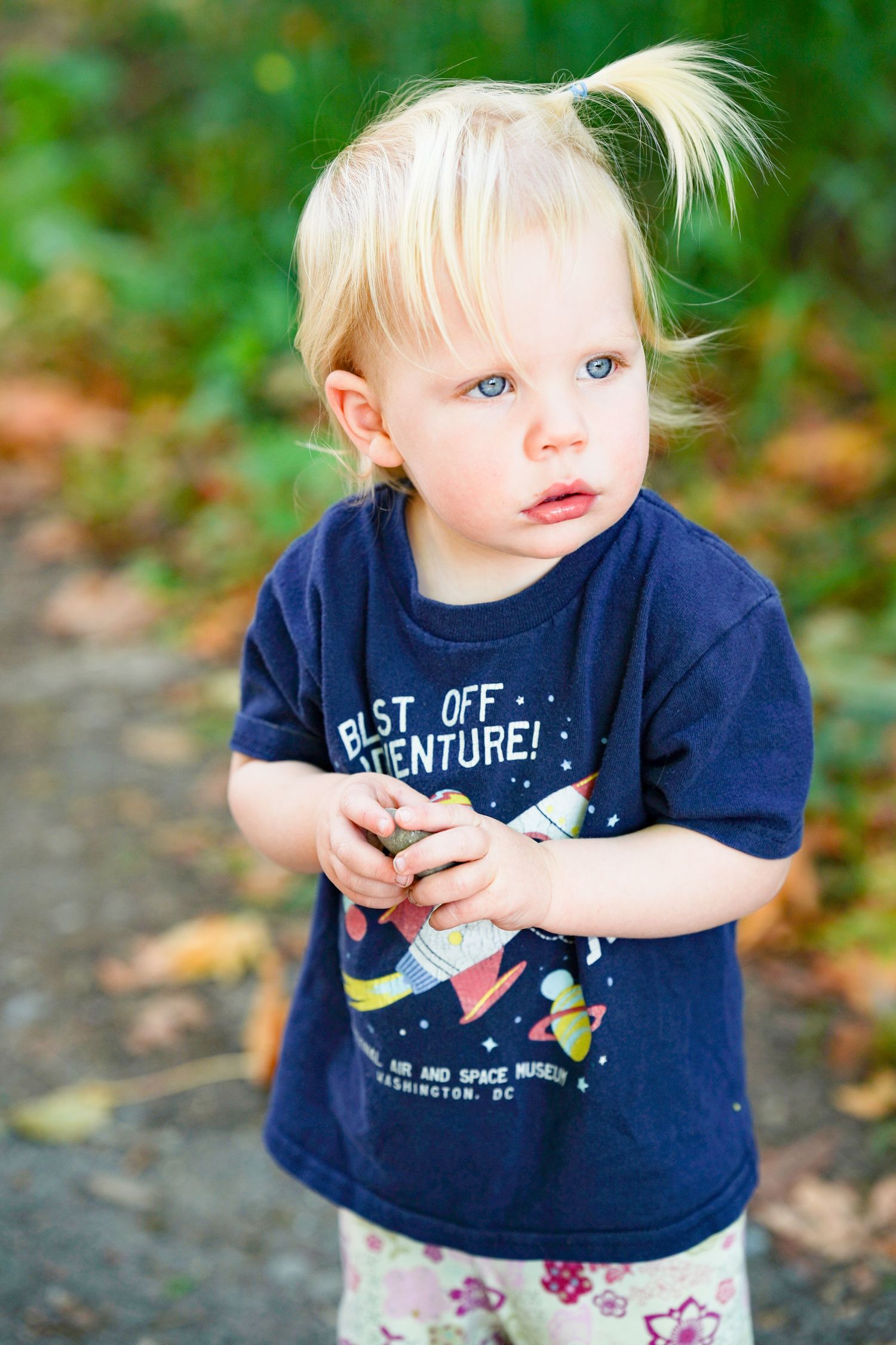 Blonde toddler with blue eyes wearing a navy NASA Air and Space Museum t-shirt standing outdoors.