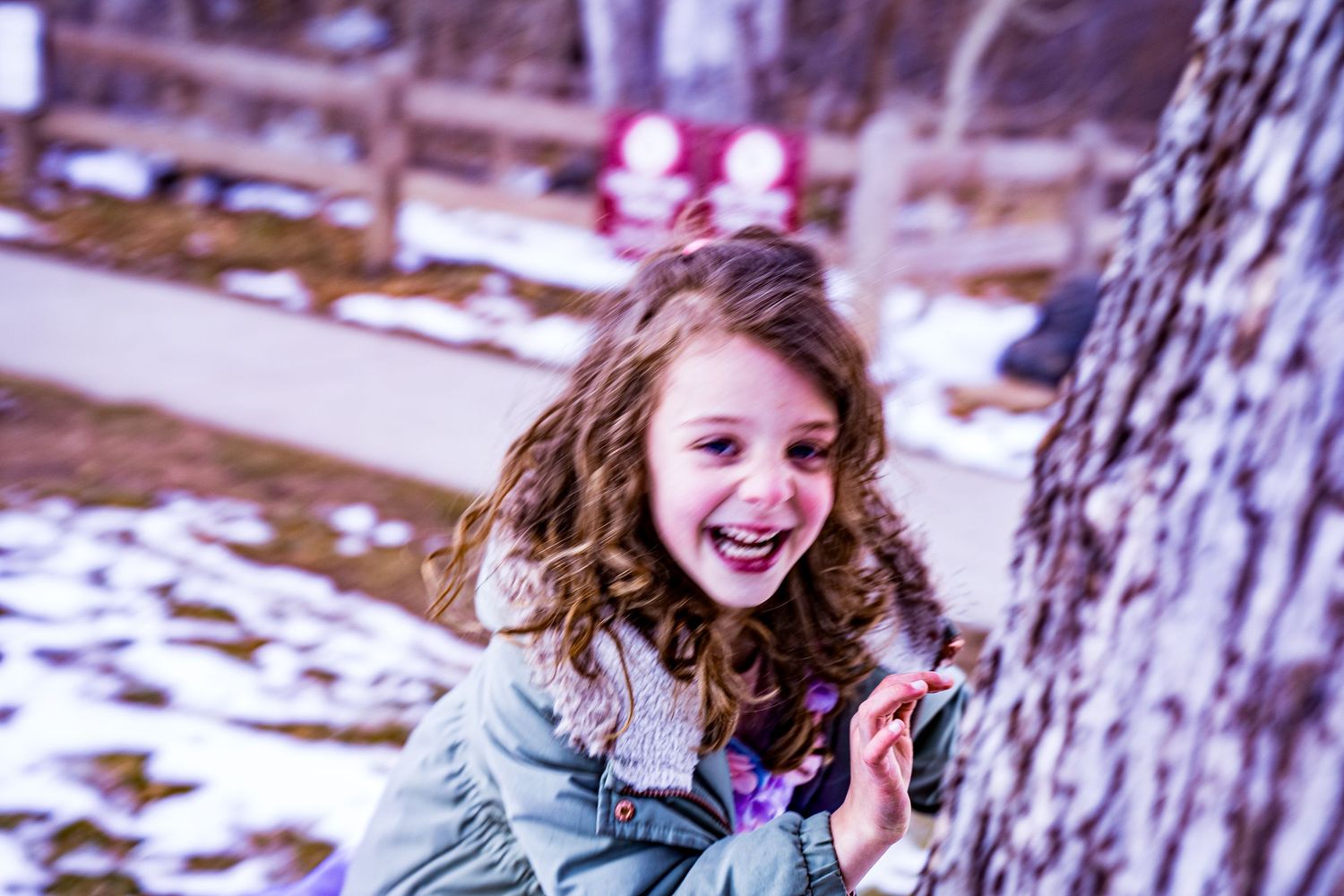 A person with curly hair laughs joyfully while sitting in a snowy winter forest setting.