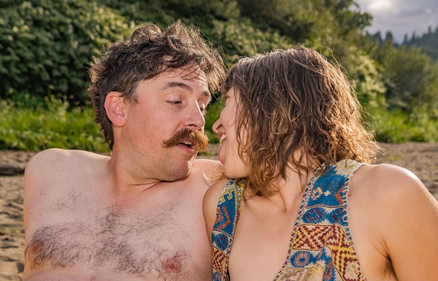 A couple sharing a romantic moment on a sandy beach surrounded by lush green trees.