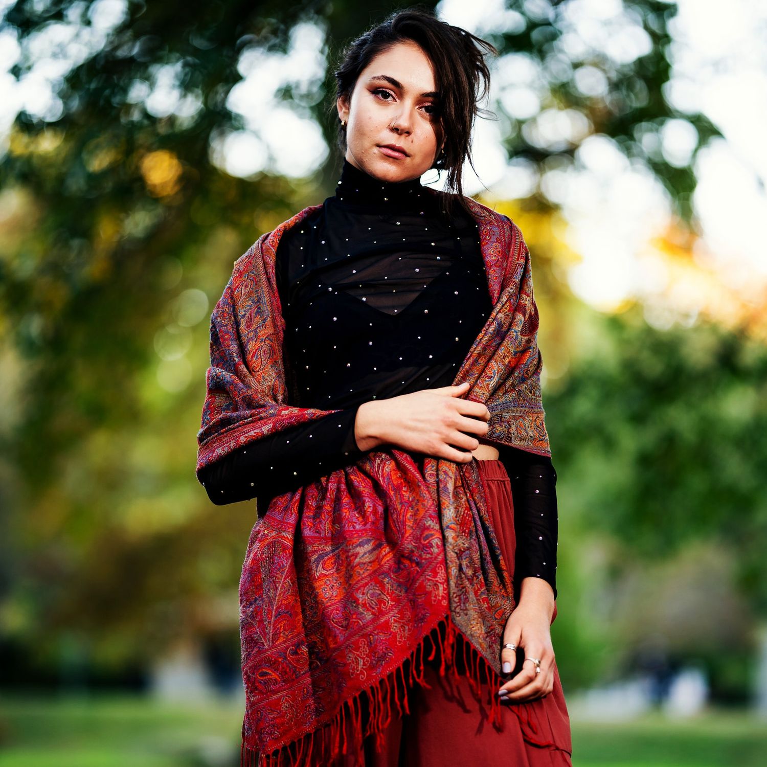 A photo of a woman with a black top and white polka dots, she has a beautiful red scarf and red pants.
