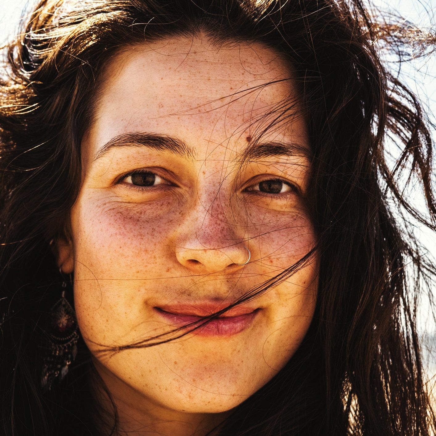 A photo of a woman looking into the camera with brown hair and brown freckles.