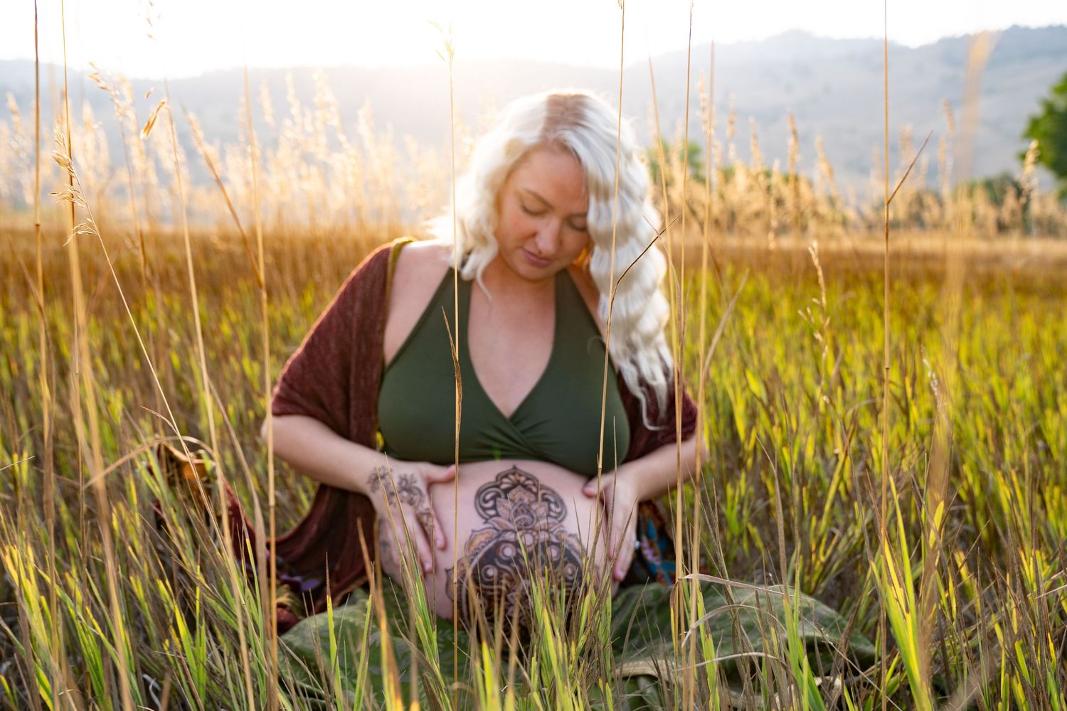 A woman in a green top stands thoughtfully in a golden field of tall grass during sunset.