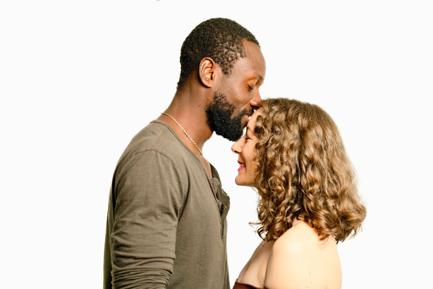 A Black man and a curly-haired woman face each other intimately, nearly touching foreheads, against a white background.