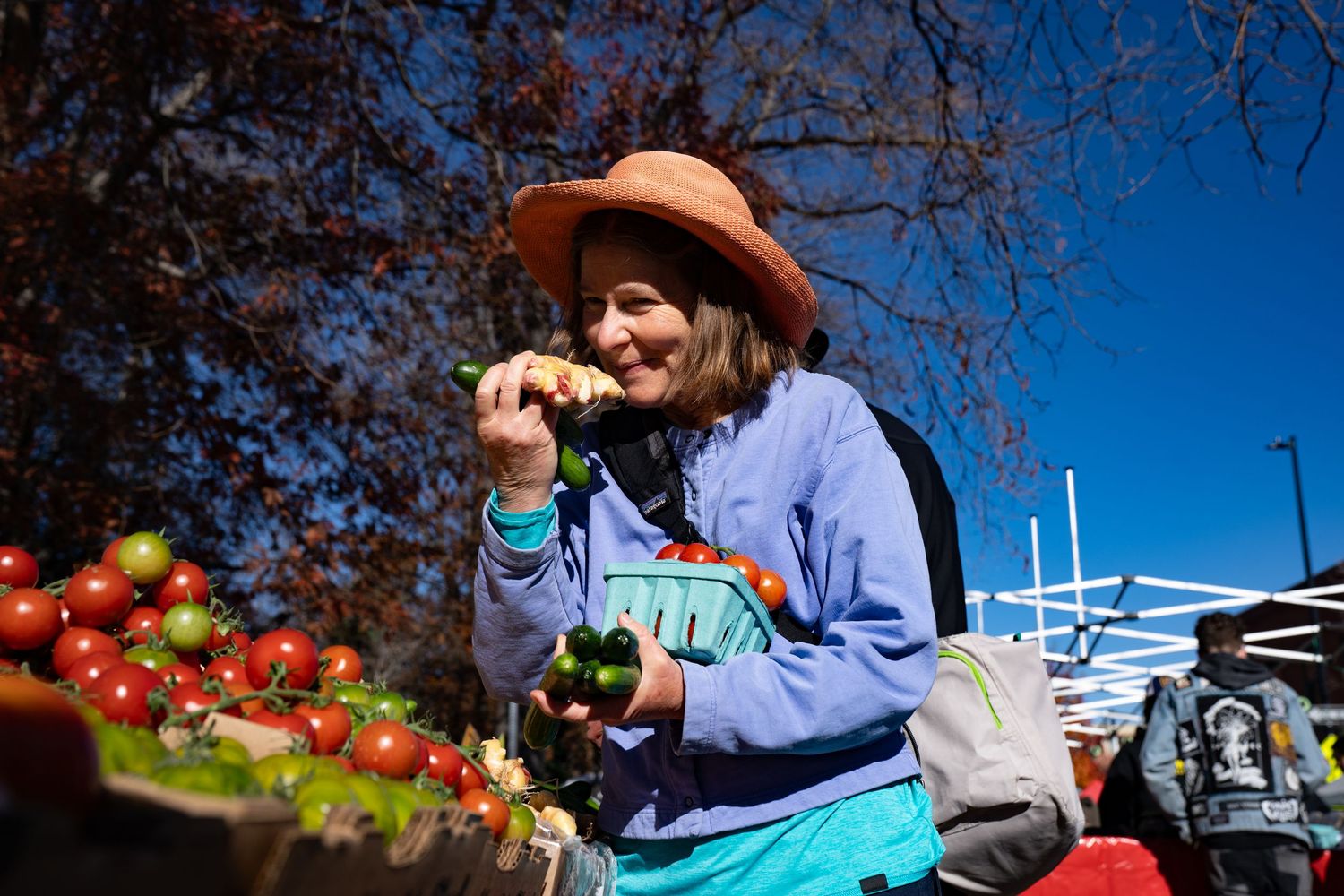 Autumn scene at a farmers market with pumpkins and produce displays under white tents.